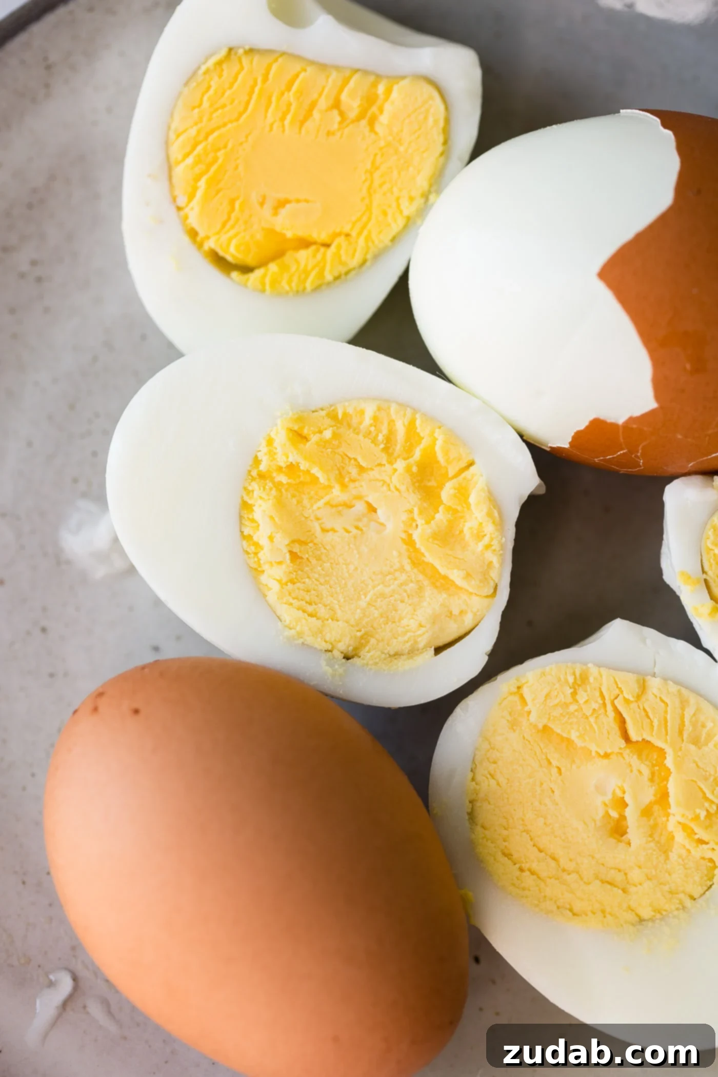 Perfectly Peeled Hard Boiled Eggs Several hard-boiled brown eggs, some fully peeled, others partially peeled, and two cut in half to showcase their perfect yolks and easy peelability.