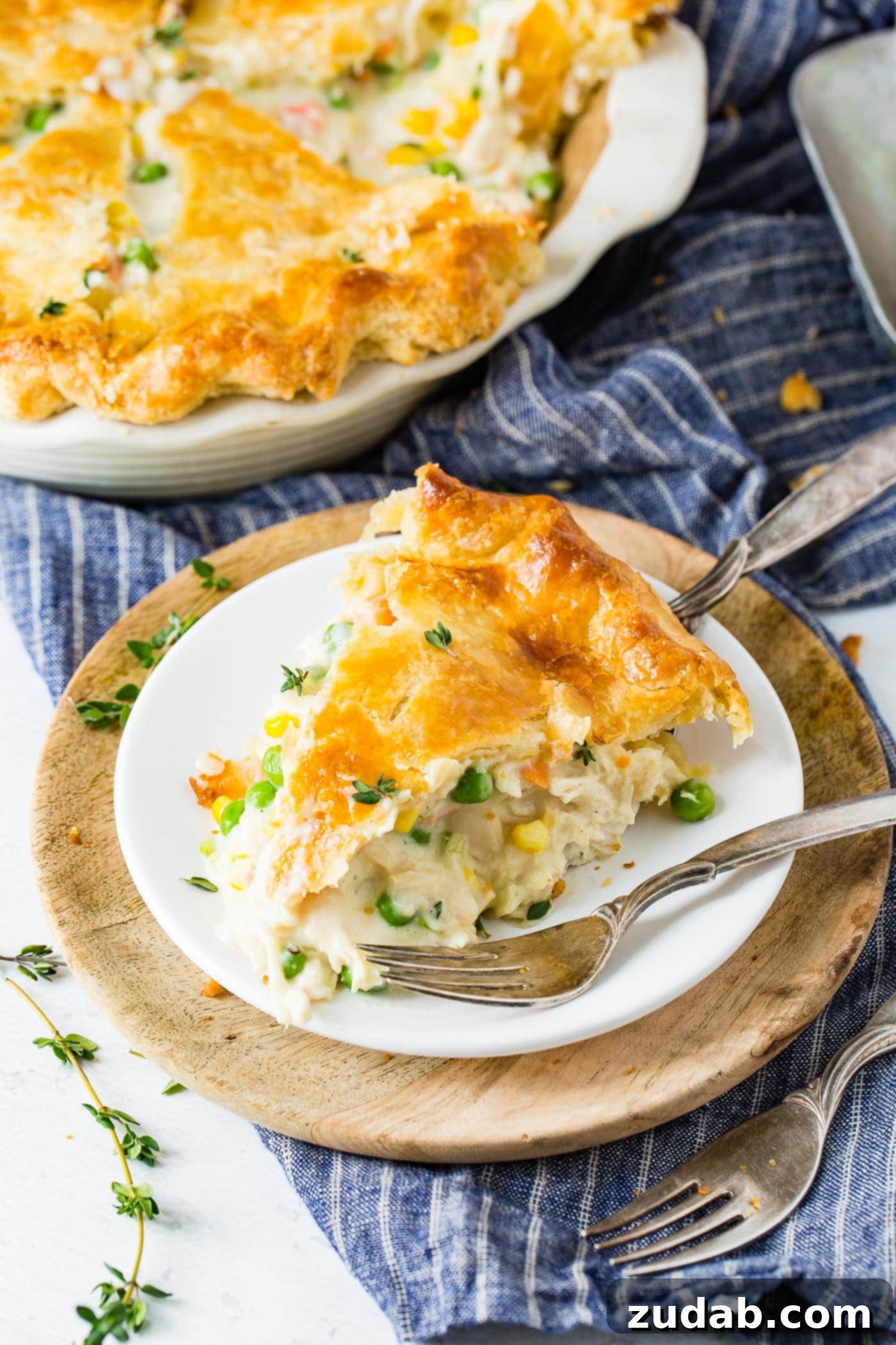 My Best Homemade Chicken Pot Pie Recipe A slice of chicken pot pie on a dinner plate with a fork resting on the plate. In the background there is a chicken pot pie in the pie dish.