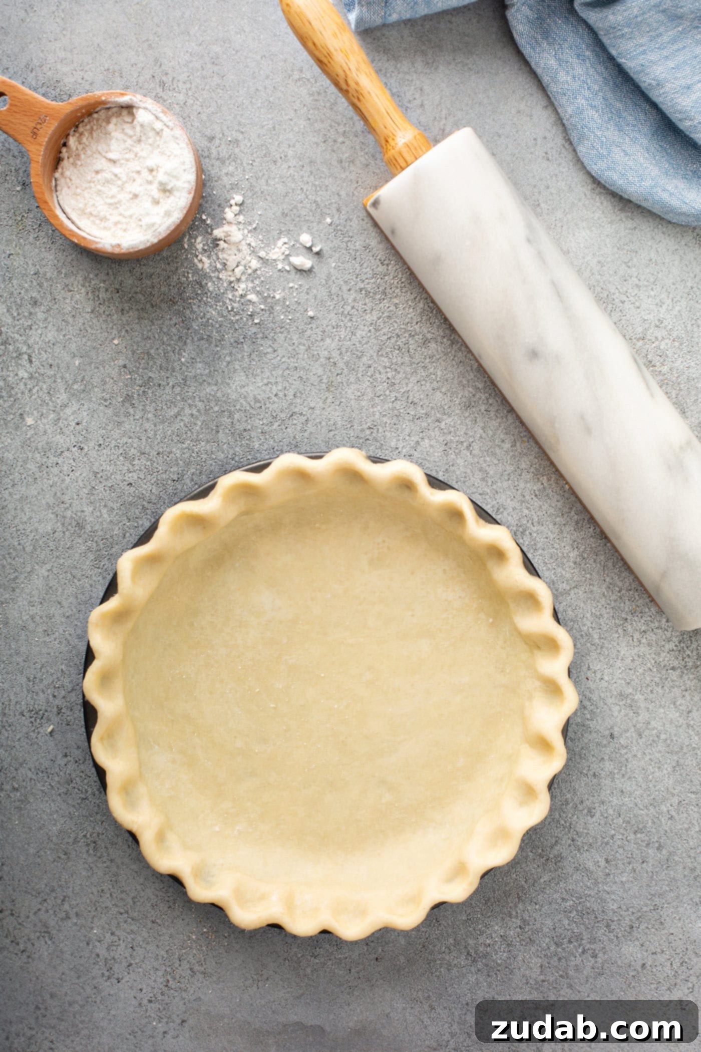 Master My Absolute Favorite Pie Crust With This Video 8 A photo of an uncooked all butter pie crust in a pie tin sitting on a table next to a rolling pin and cup of flour.