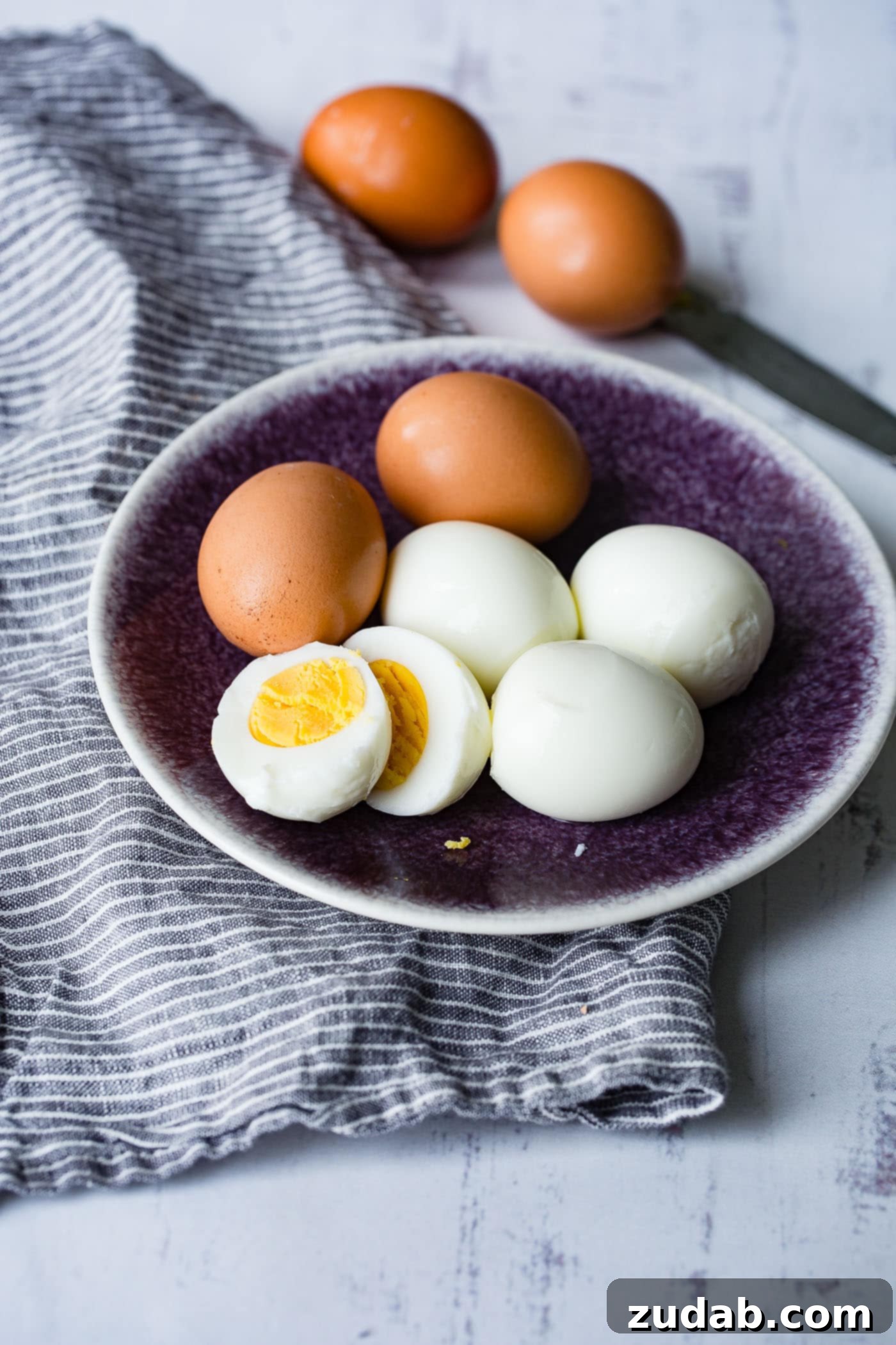 Instant Pot Hard Boiled Eggs A plate with 6 hard boiled eggs. There are two brown eggs, three that have been peeled and one that is peeled and cut in half with a perfectly cooked yolk.
