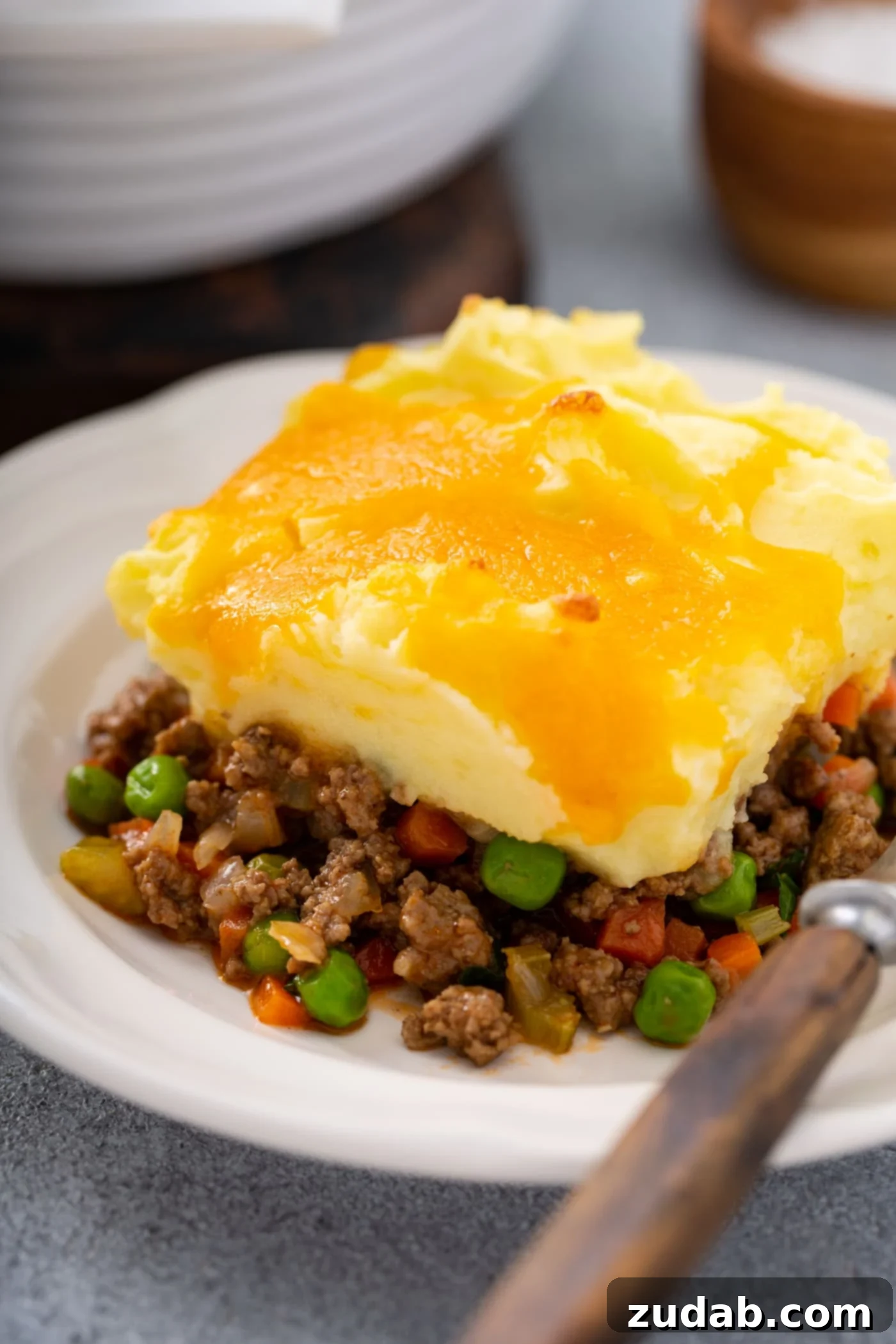 Classic Shepherd's Pie A serving of shepherd's pie on a white plate. there is a fork resting next to it on the plate.