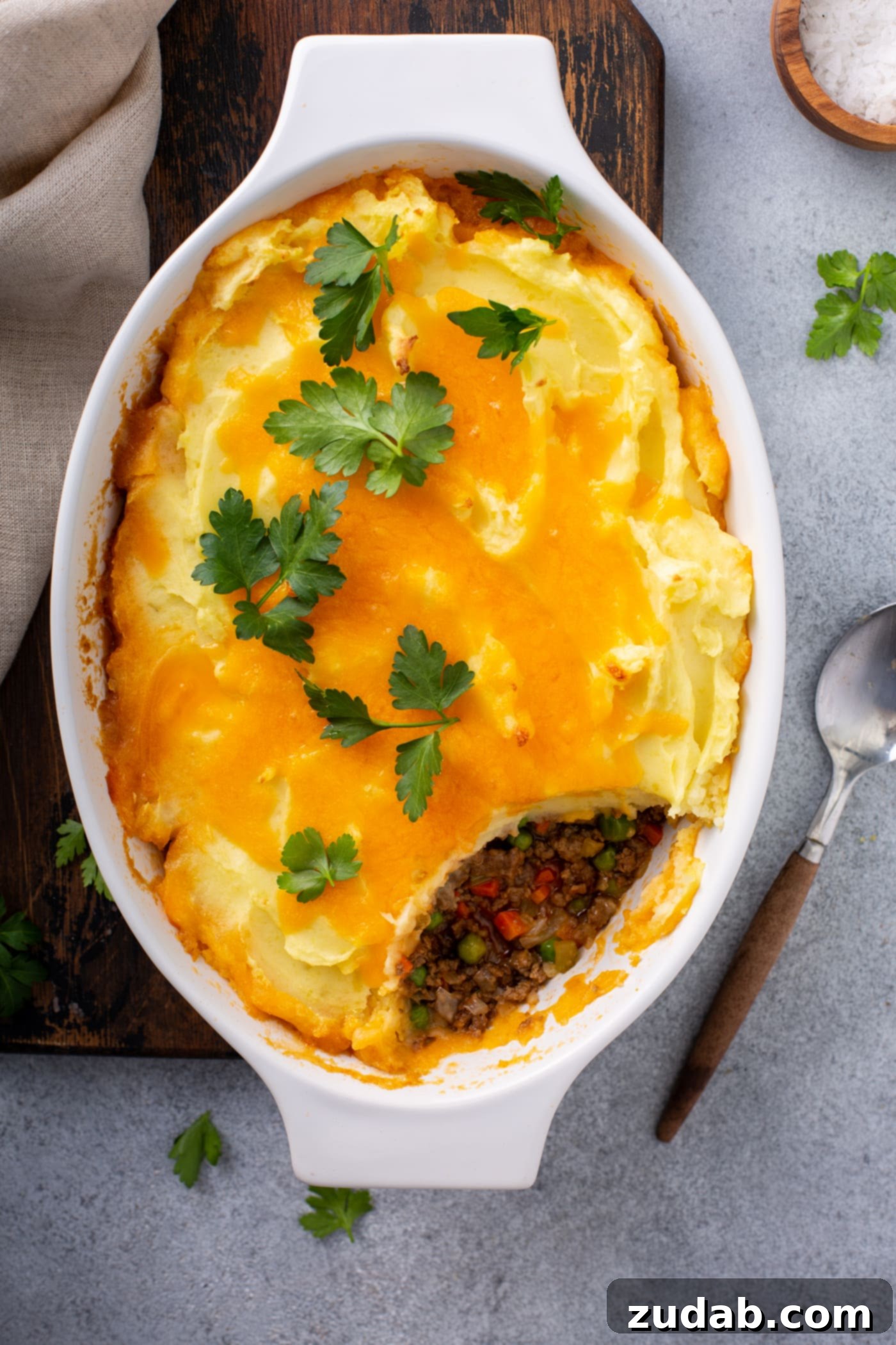 Classic Shepherd's Pie A casserole dish of shepherd's pie. A serving has been removed so you can see the ground beef, carrots and peas in the filling. It is topped with mashed potatoes and melted cheese with a few parsley leaves on top.