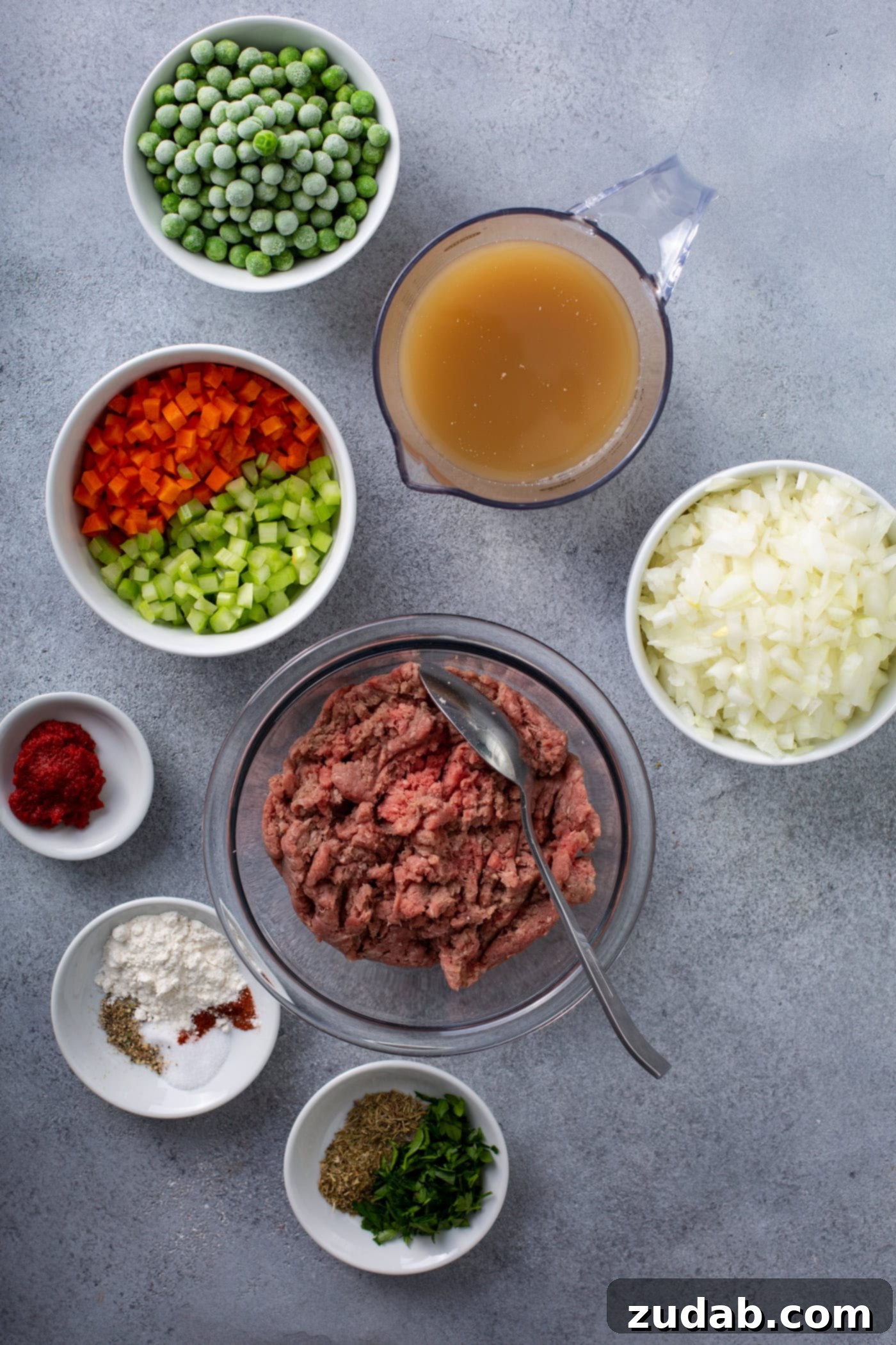 Classic Shepherd's Pie A table top with containers of ground beef, onions, chopped red and green peppers, spices, peas, and broth.