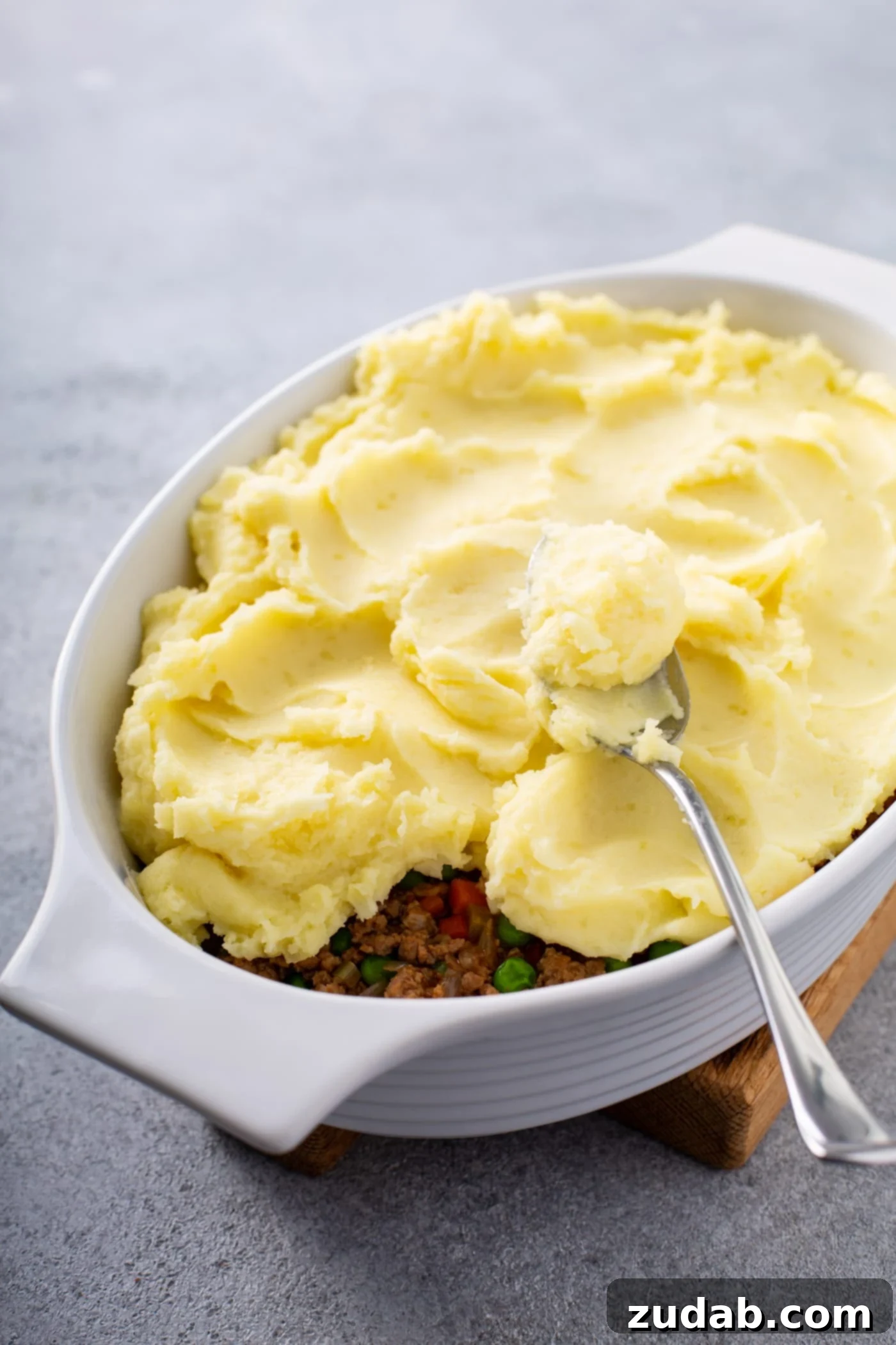 Classic Shepherd's Pie A casserole dish filled with shepherd's pie filling and topped with mashed potatoes. There is a spoon resting on top.