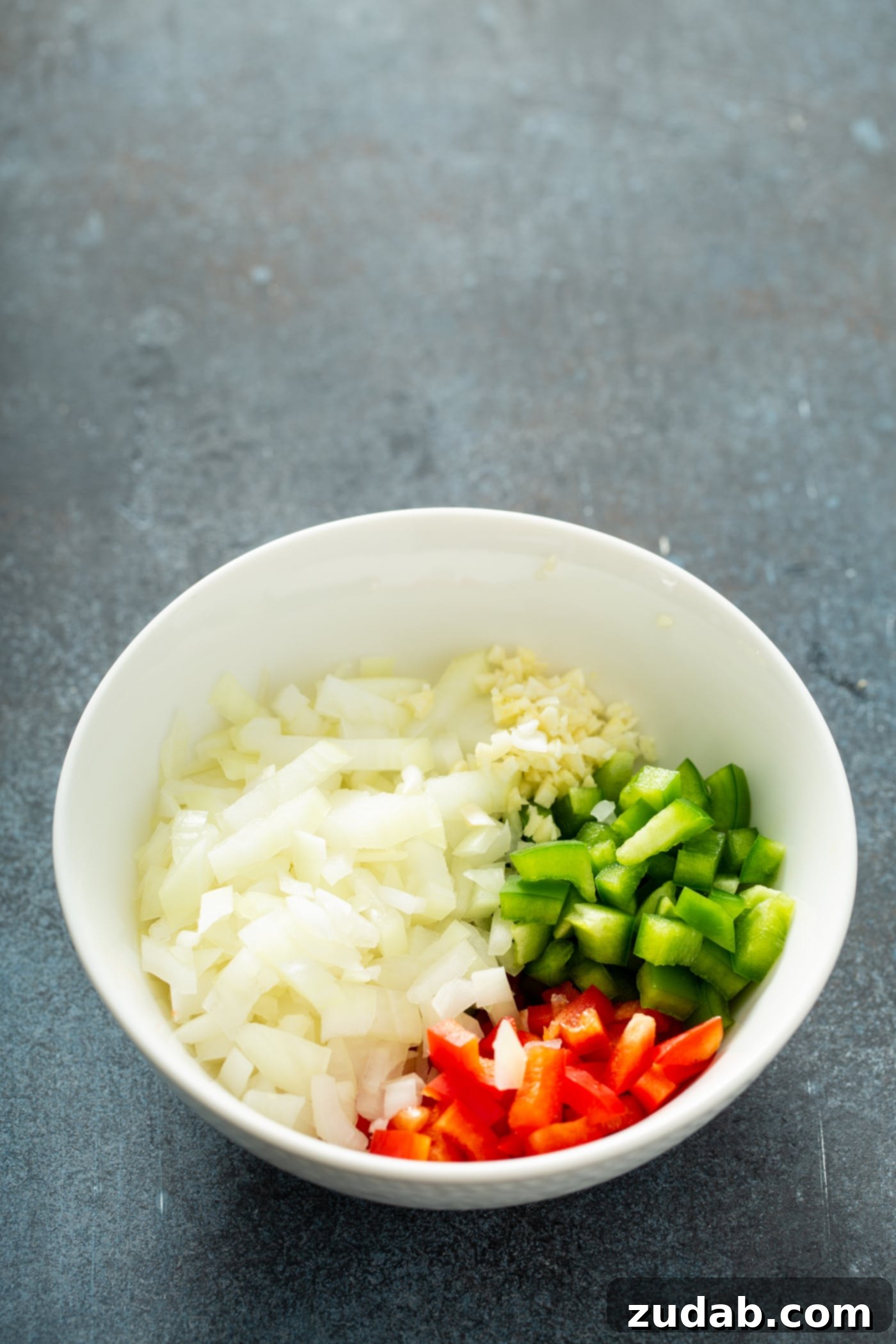 Your New Favorite Homemade Black Bean Burger 5 A white bowl with finely chopped onions, and a vibrant mix of chopped red and green bell peppers, ready to be cooked.