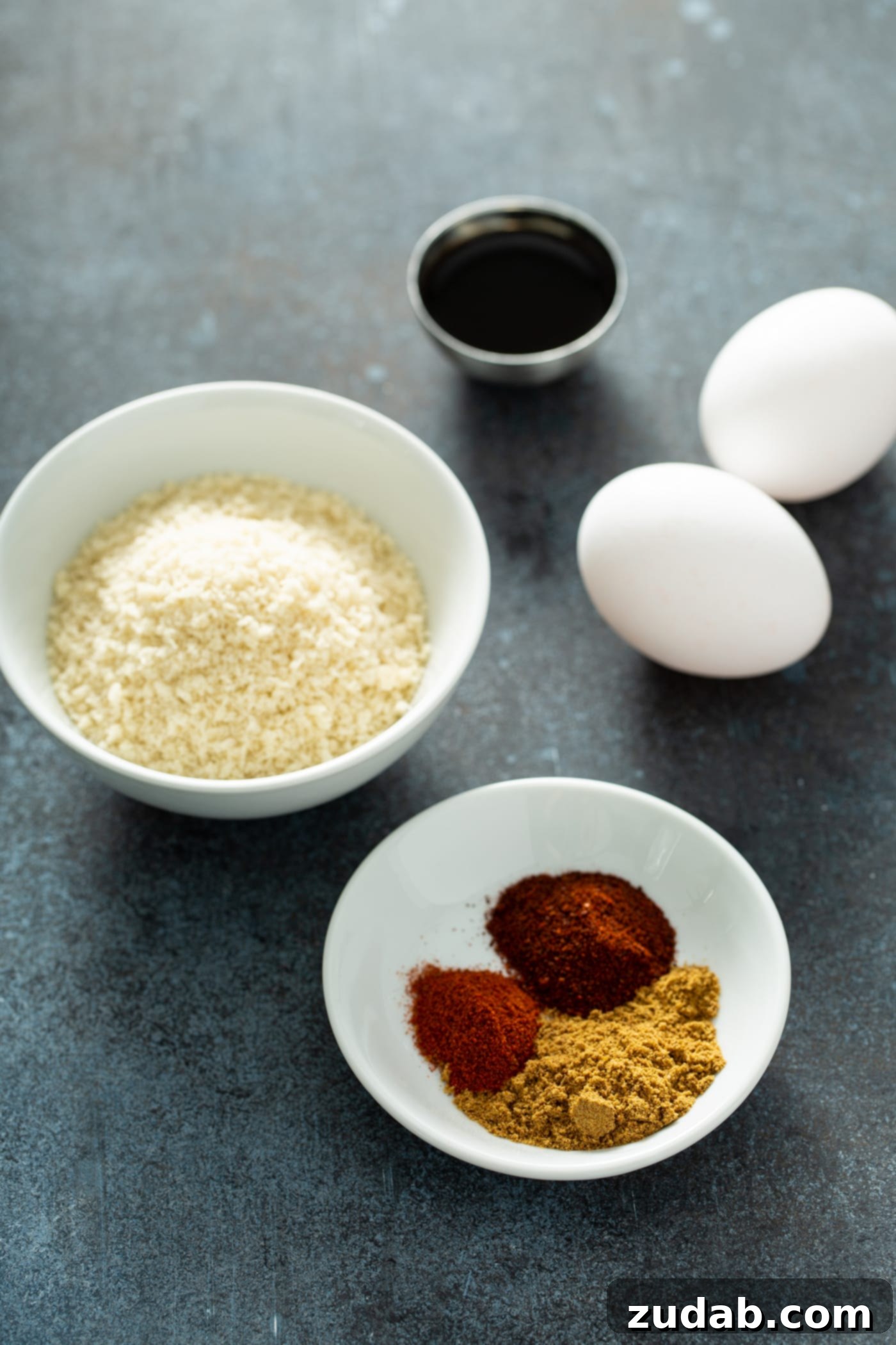 Your New Favorite Homemade Black Bean Burger 6 A white bowl with crunchy bread crumbs, another white bowl holding a vibrant blend of cumin, paprika and chili powder, two fresh white eggs, and a small container of Worcestershire Sauce, all essential ingredients for the black bean burger.