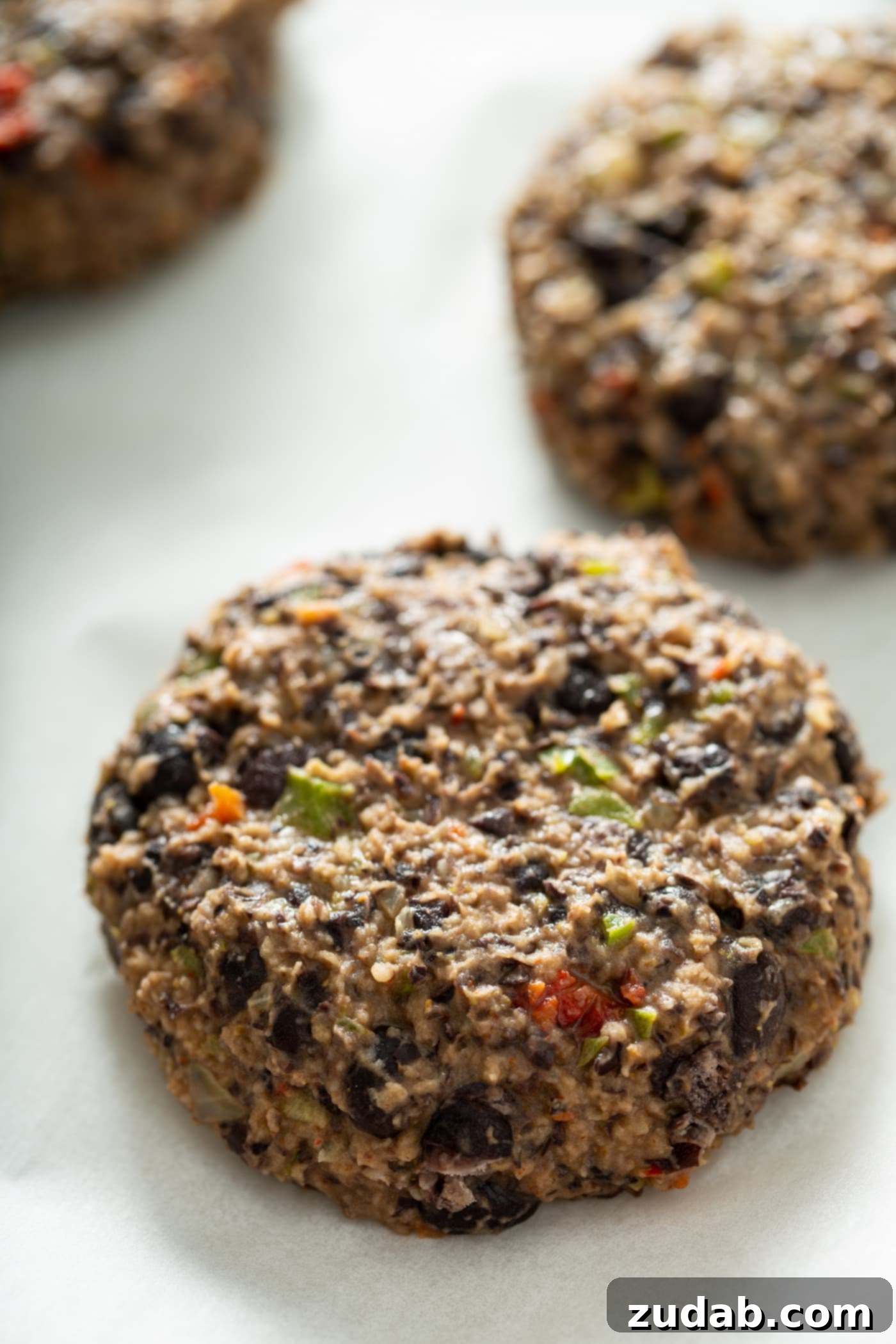 Your New Favorite Homemade Black Bean Burger 8 An uncooked black bean burger patty, perfectly formed and ready for cooking, with another patty blurred in the background.
