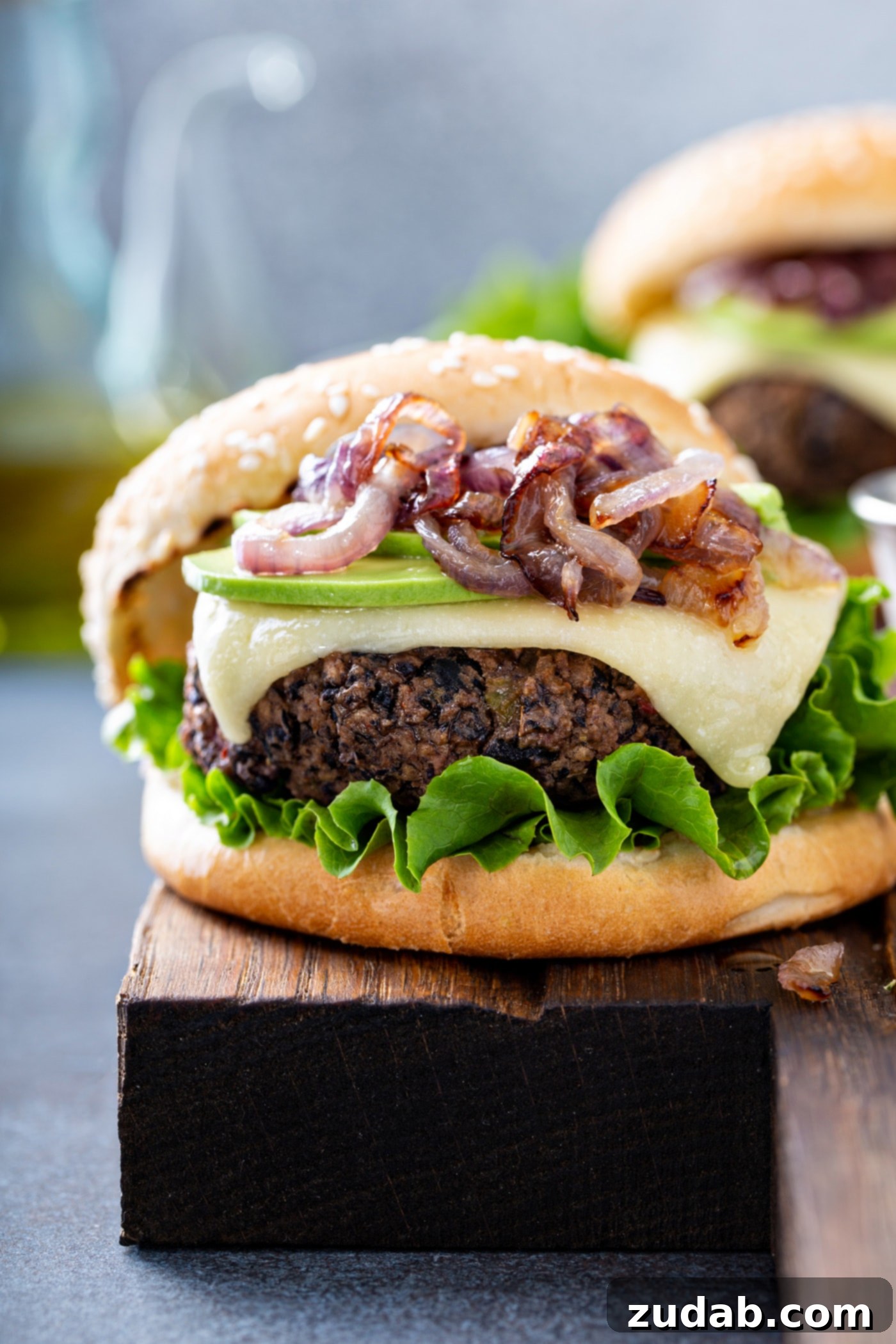 Your New Favorite Homemade Black Bean Burger 10 A close-up shot of a black bean burger on a sesame seed bun, expertly topped with fresh onions, creamy avocado, melted cheese, and crisp lettuce, highlighting its delicious layers.