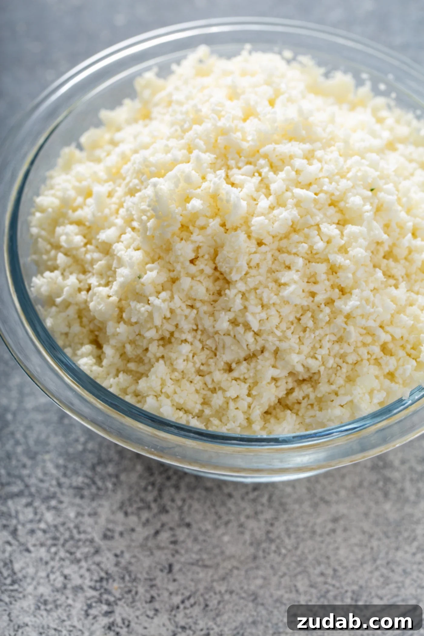 Hand-Grated Cauliflower Rice: A Simple Alternative A clear glass bowl showcasing freshly made cauliflower rice, ready for cooking.
