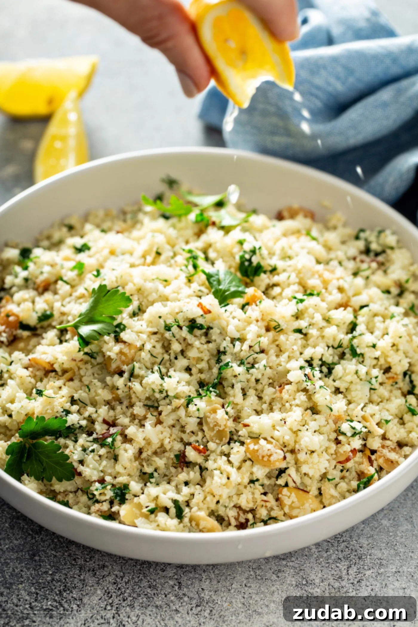Freshly Made Garlic Herb Cauliflower Rice A white serving bowl with garlic herb cauliflower rice. It's garnished with vibrant green herbs, subtle hints of garlic, and sliced almonds, with fresh parsley leaves scattered on top. This is the finished healthy side dish.