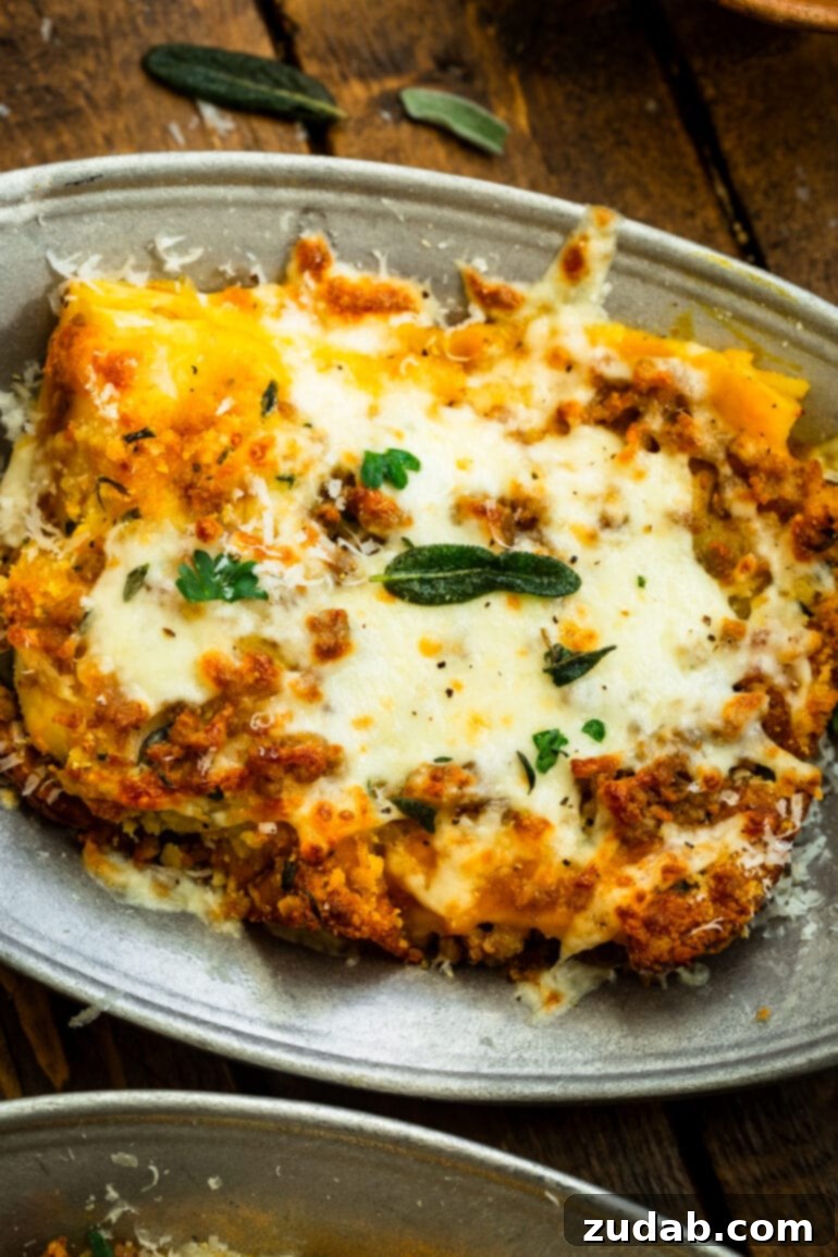 a photo of a serving of pork and butternut squash lasagna on a plate topped with melted cheese and crispy sage leaves.