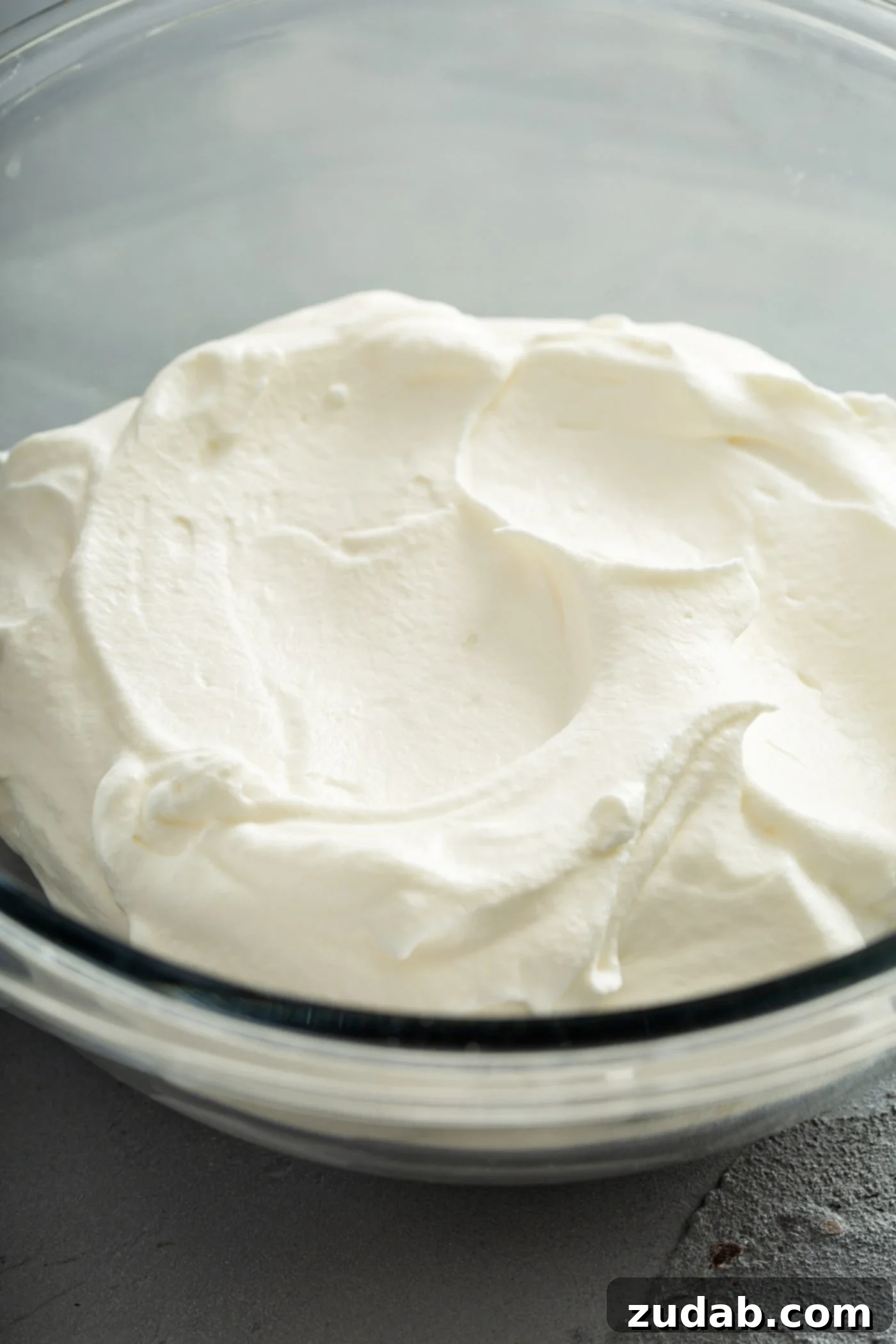 Simply Delicious Homemade Whipped Cream 4 A charming close-up of a glass bowl brimming with freshly made whipped cream, its peaks and swirls perfectly formed, inviting a taste. The image highlights the ideal consistency and sweetness of the homemade dessert topping.