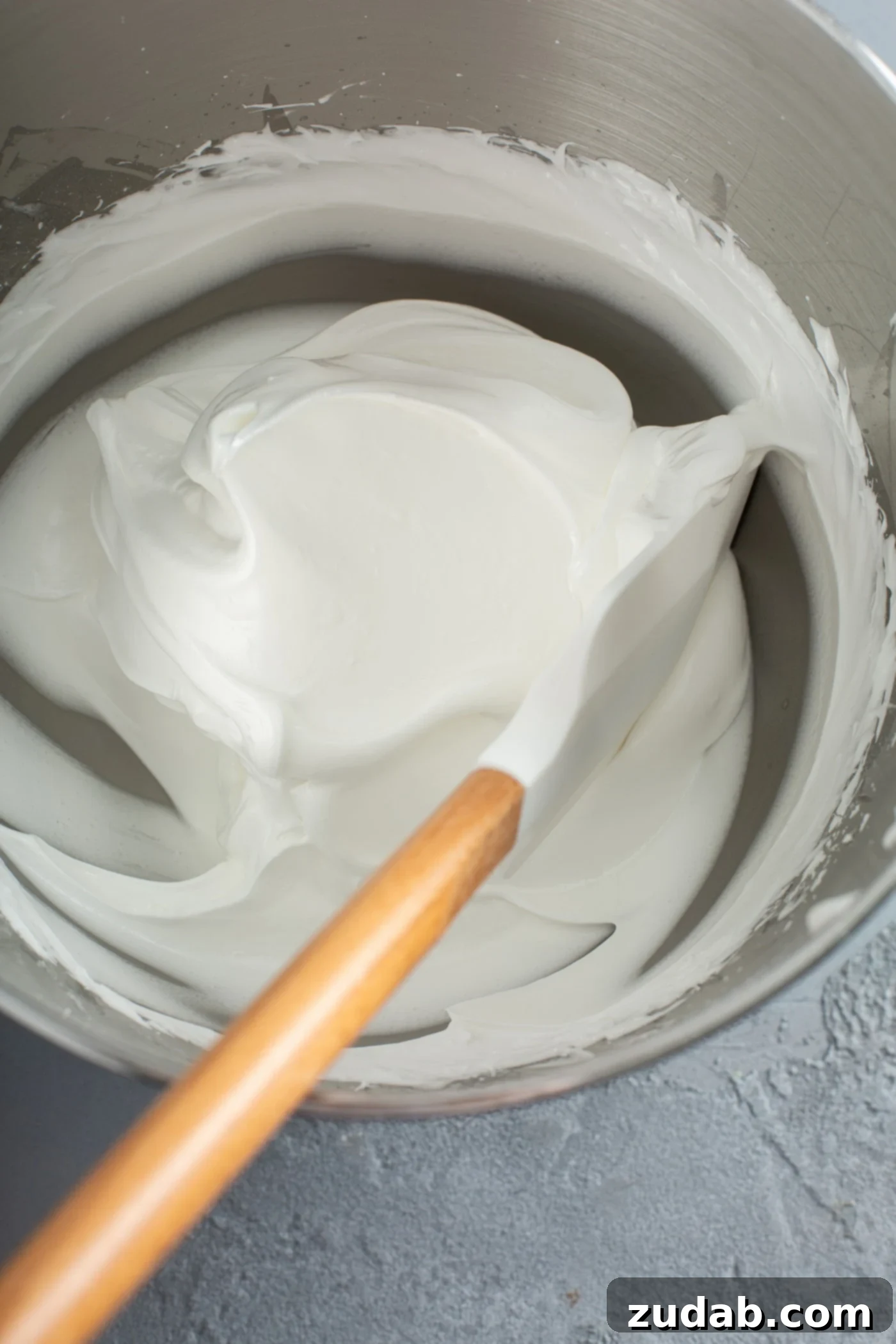 A mixing bowl with stiff meringue and a spatula inside.