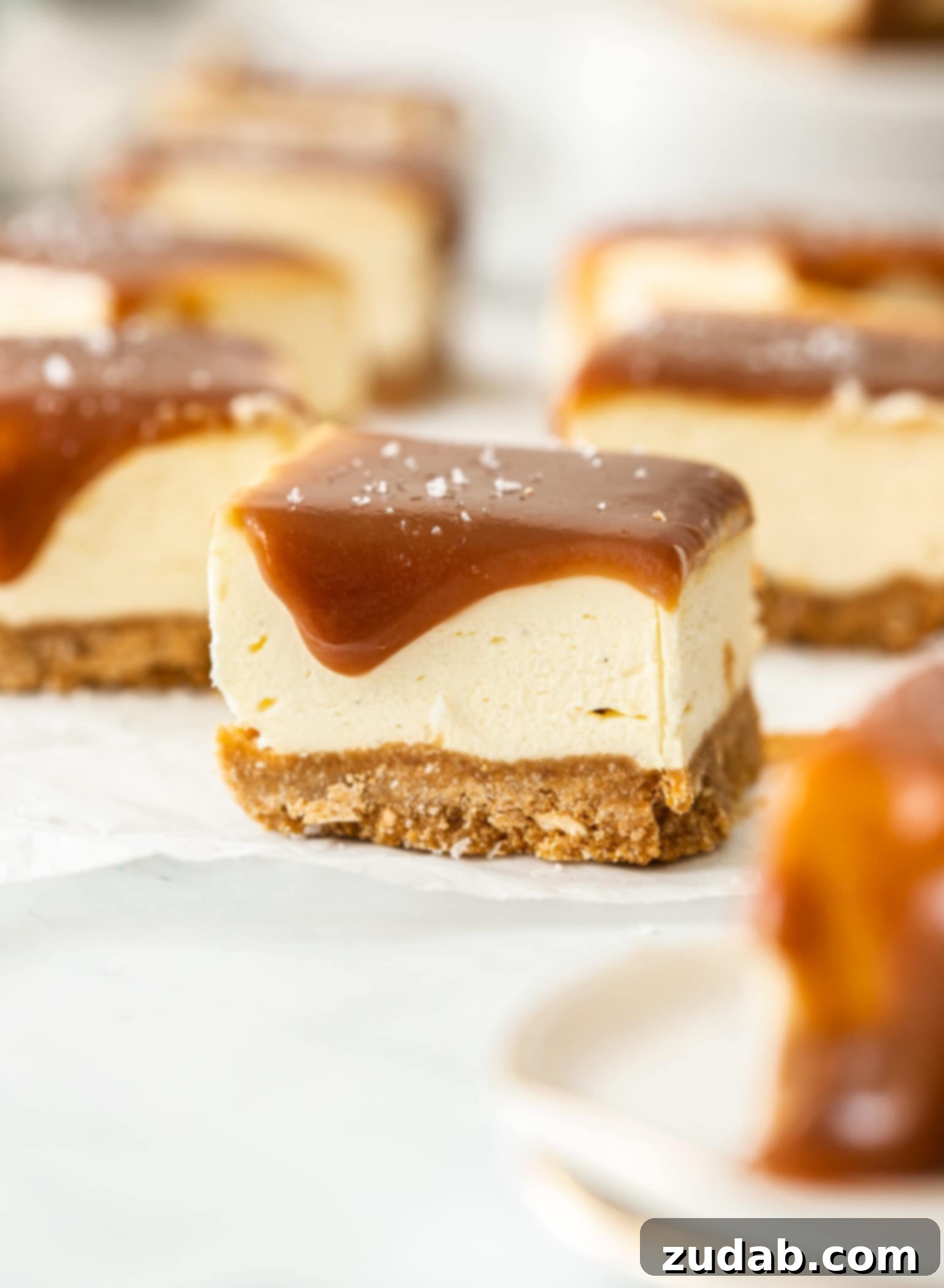 Effortless Caramel Bliss Bars 3 A close-up view of a single No-Bake Caramel Cheesecake Bar, showcasing its gooey caramel topping and creamy layers on white baking paper