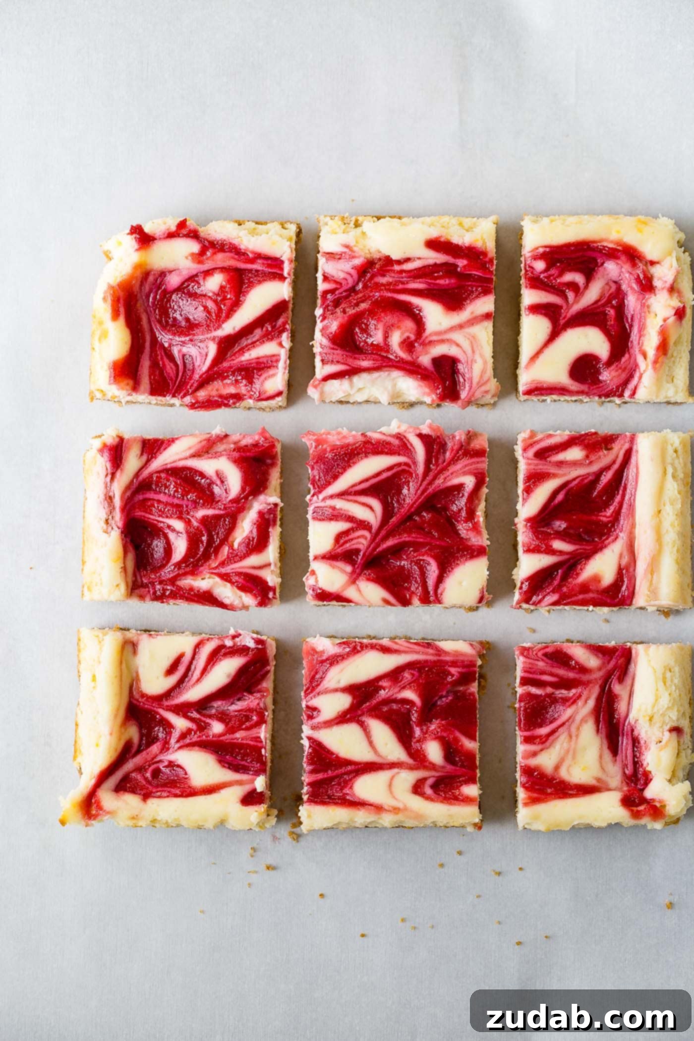 Zesty Berry Cheesecake Swirls 2 Nine perfectly cut squares of swirled raspberry lemon cheesecake bars, showcasing a golden-brown graham cracker crust, a dense and creamy lemon cheesecake filling, and a beautiful raspberry sauce swirled artfully on top. The vibrant colors highlight the fresh ingredients.