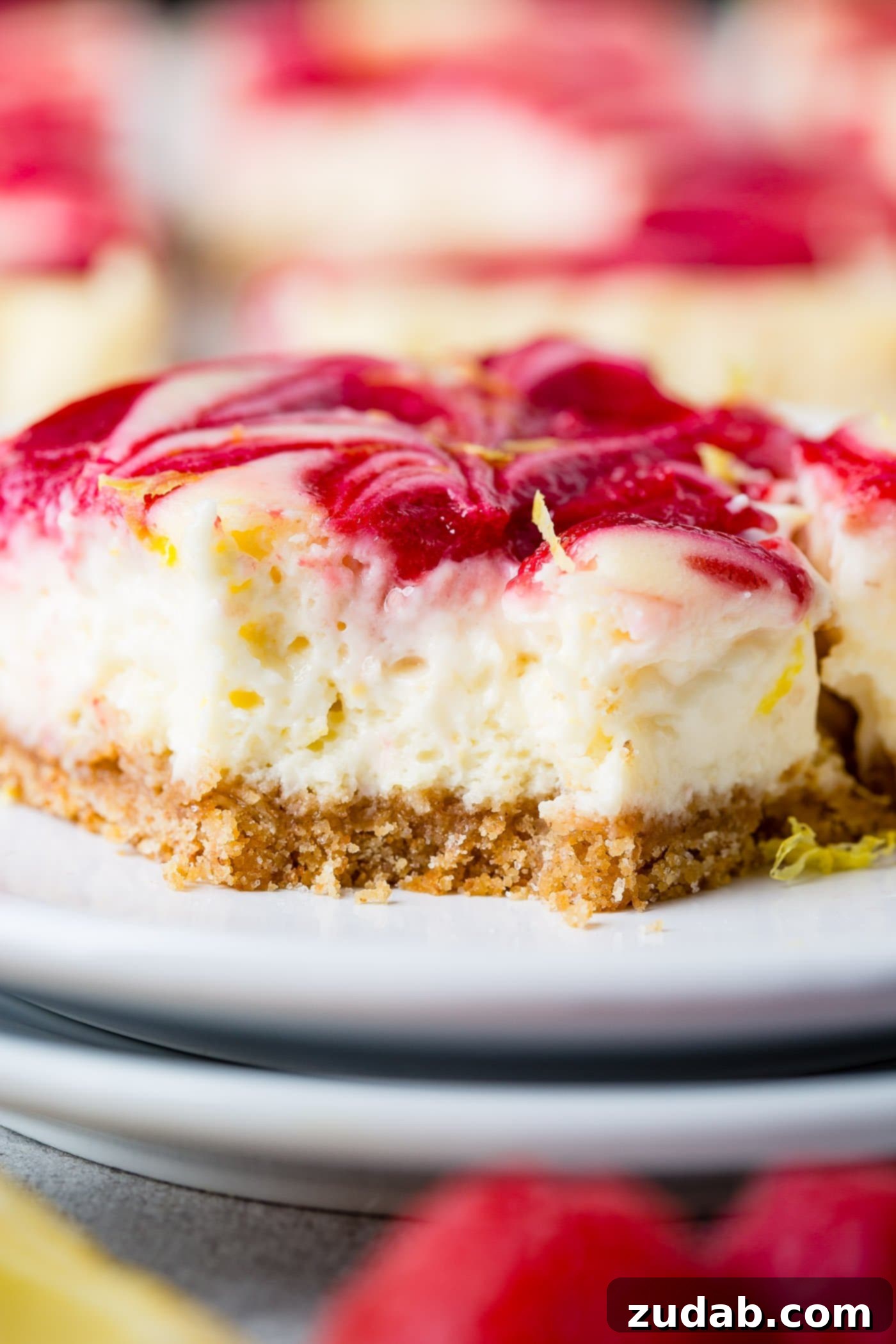 Zesty Berry Cheesecake Swirls 7 A close-up view of a single swirled raspberry lemon cheesecake bar, highlighting its creamy lemon cheesecake texture, the crispy graham cracker crust at the base, and the beautiful, artistic swirls of vibrant raspberry sauce on the top surface. The image emphasizes the rich and inviting details of the dessert.