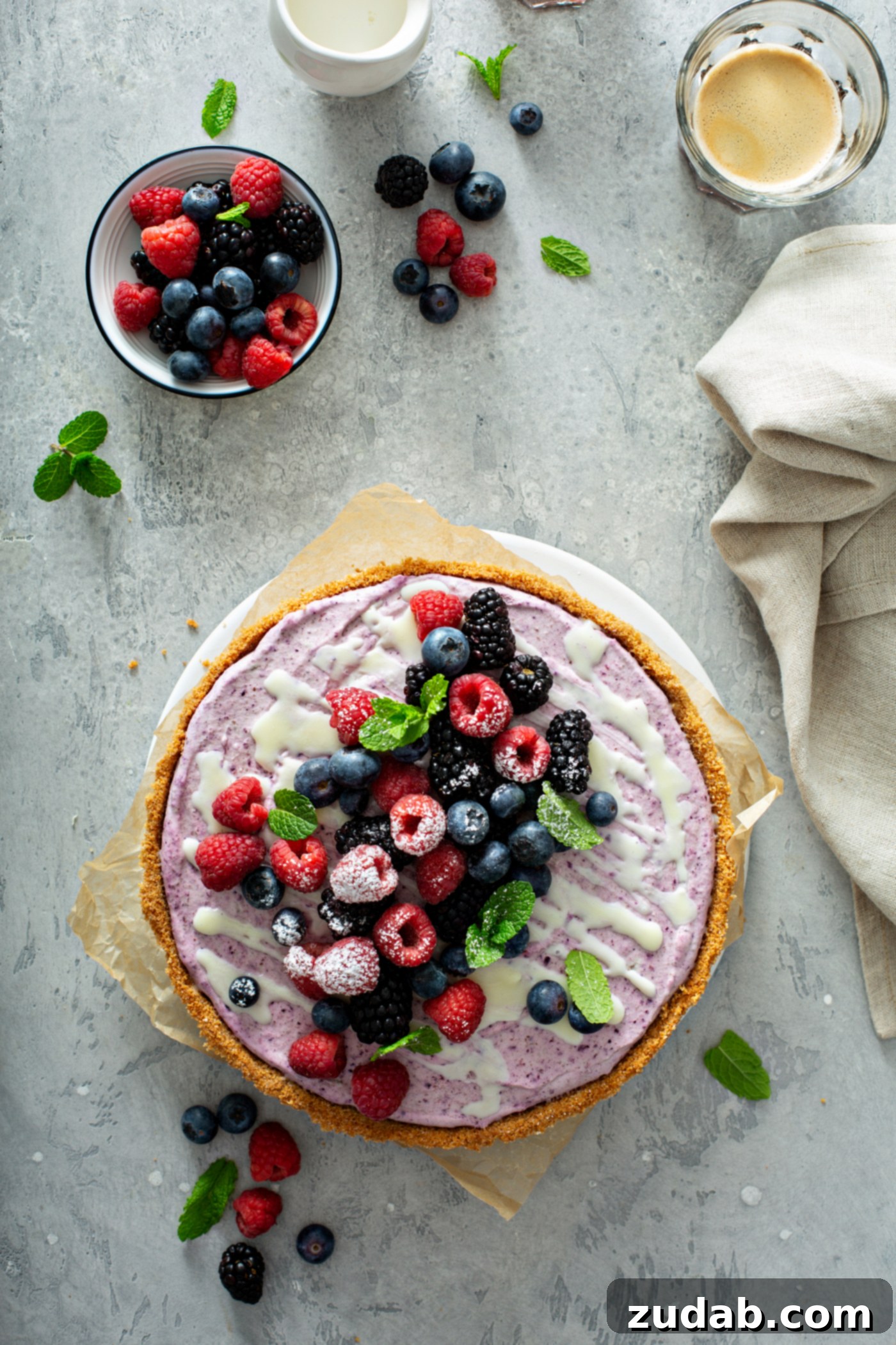 White Chocolate Berry Icebox Pie 12 A whole white chocolate berry pie with mixed berries on top. There are mint leaves sprinkled on top of the berries and on the table top. A bowl of mixed berries and a napkin are in the background.