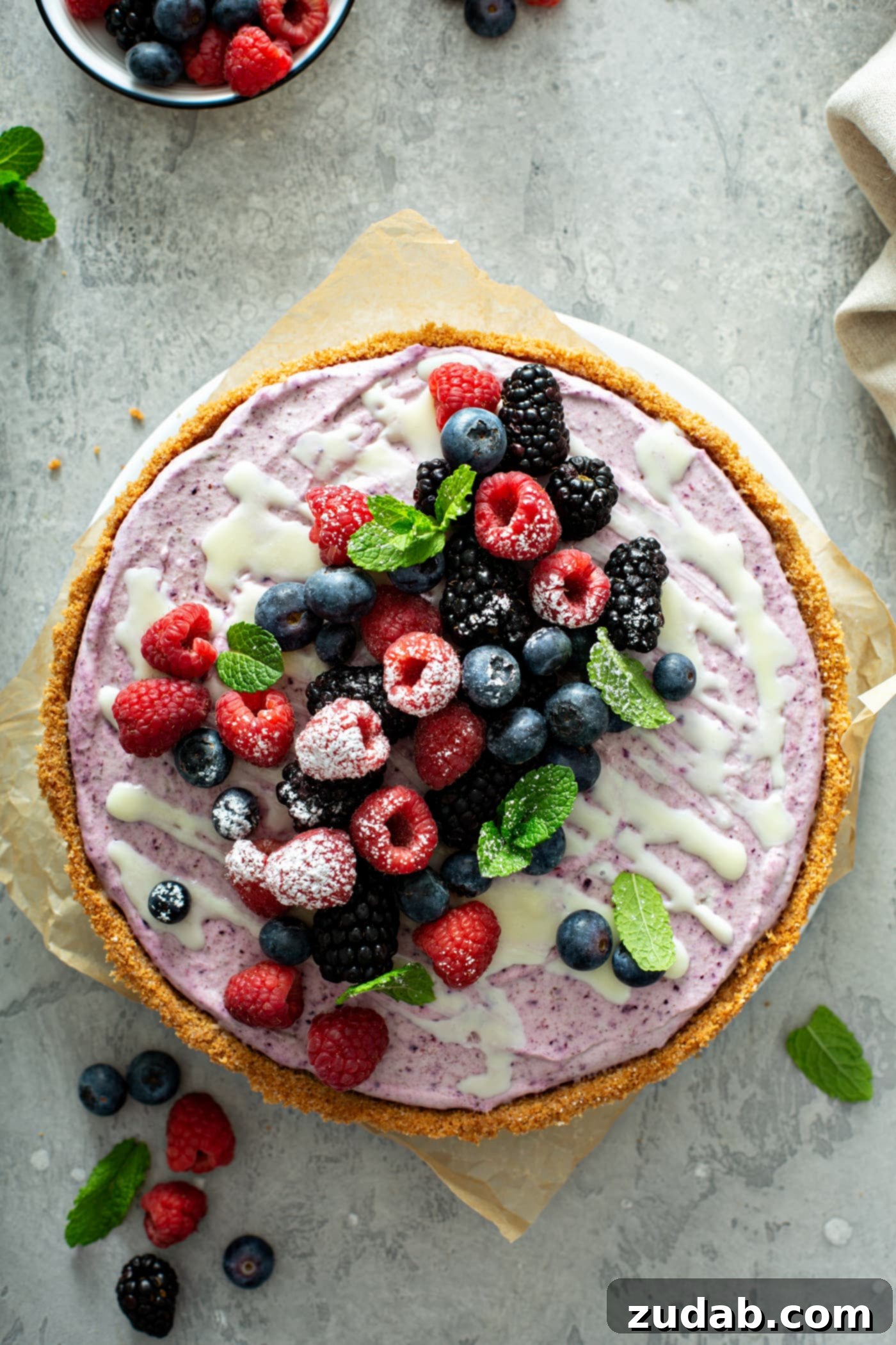 White Chocolate Berry Icebox Pie 13 A whole white chocolate berry pie with mixed berries and mint leaves on top. A white chocolate sauce is drizzled over the top of the pie.