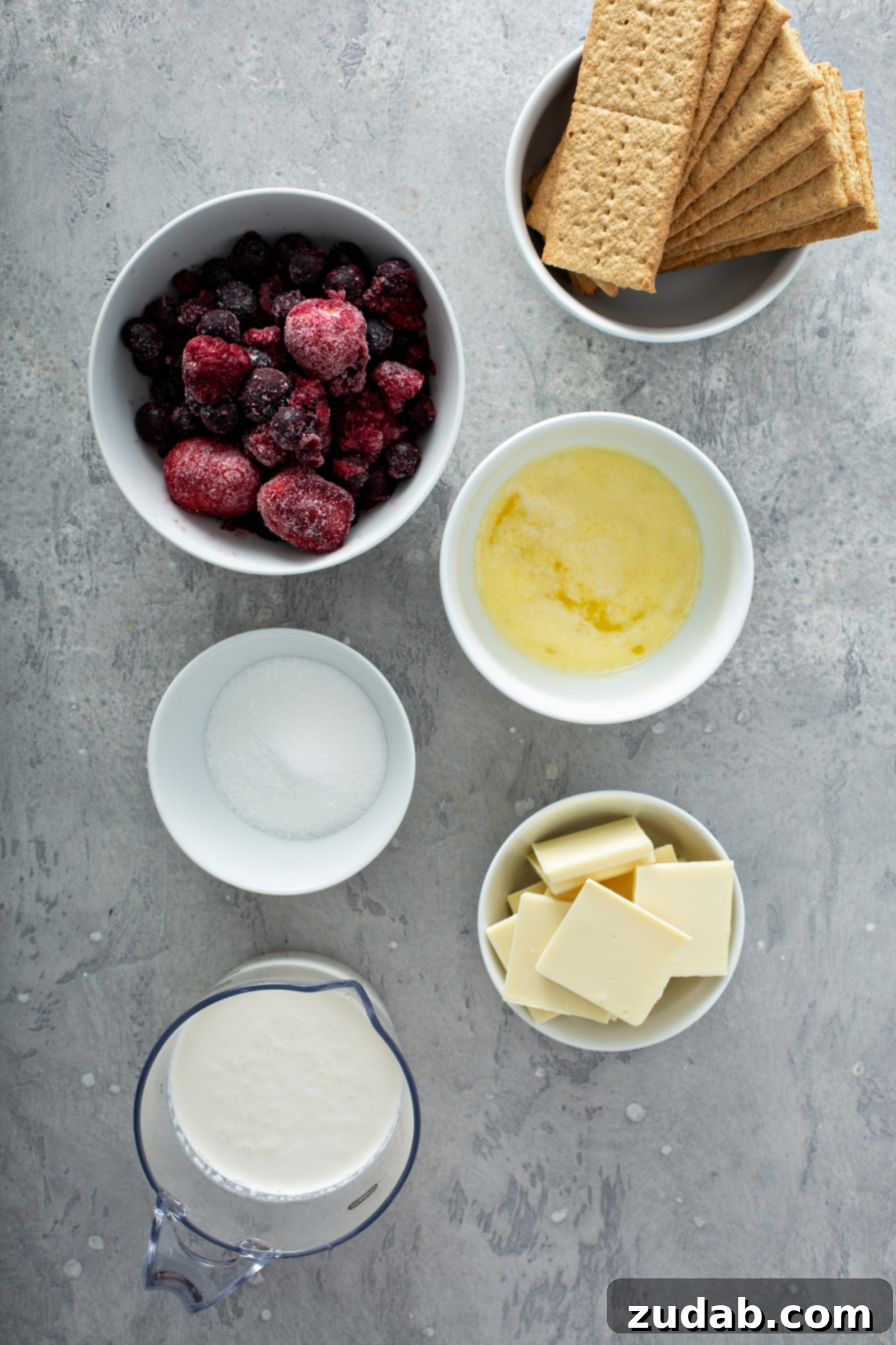 White Chocolate Berry Icebox Pie 5 Small containers of ingredients for white chocolate berry pie. There are containers of butter, cubes of white chocolate, berries, graham crackers, sugar, and whipped cream.