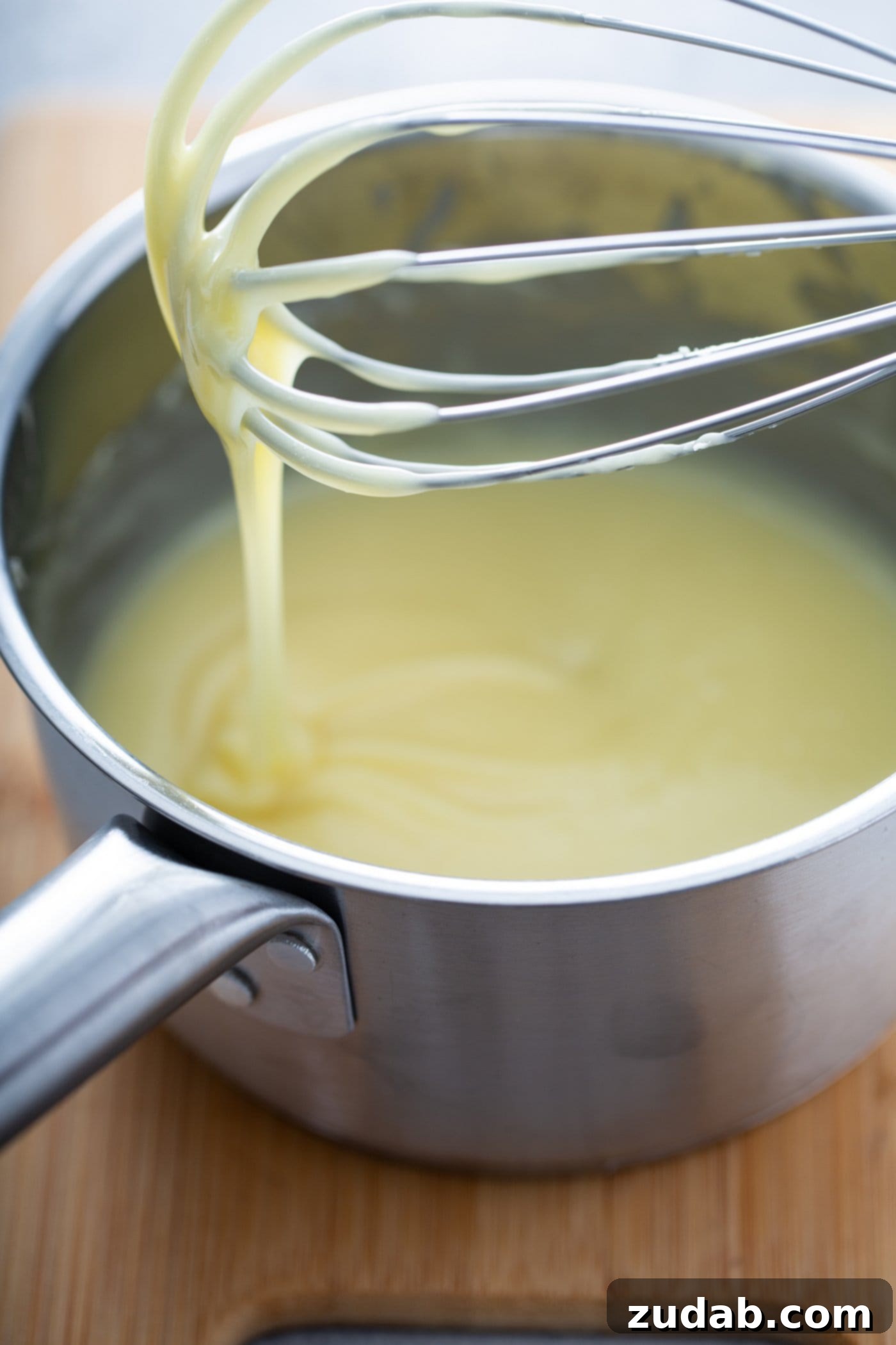 White Chocolate Berry Icebox Pie 7 A pot with melted white chocolate. A whisk with white chocolate dripping from the end is held above the pot.