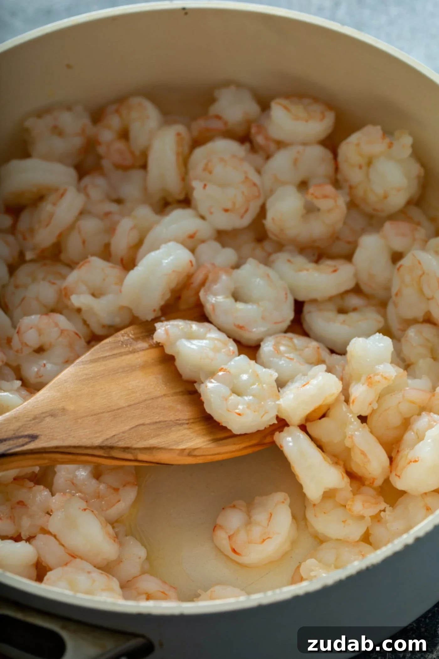Searing Shrimp for Lemon Garlic Shrimp A close-up shot of seasoned shrimp sizzling in a skillet, turning pink as they cook. A wooden spoon gently lifts a scoop of shrimp, showcasing their perfectly cooked texture and vibrant color, ready to be set aside for the next step of the lemon garlic shrimp recipe.