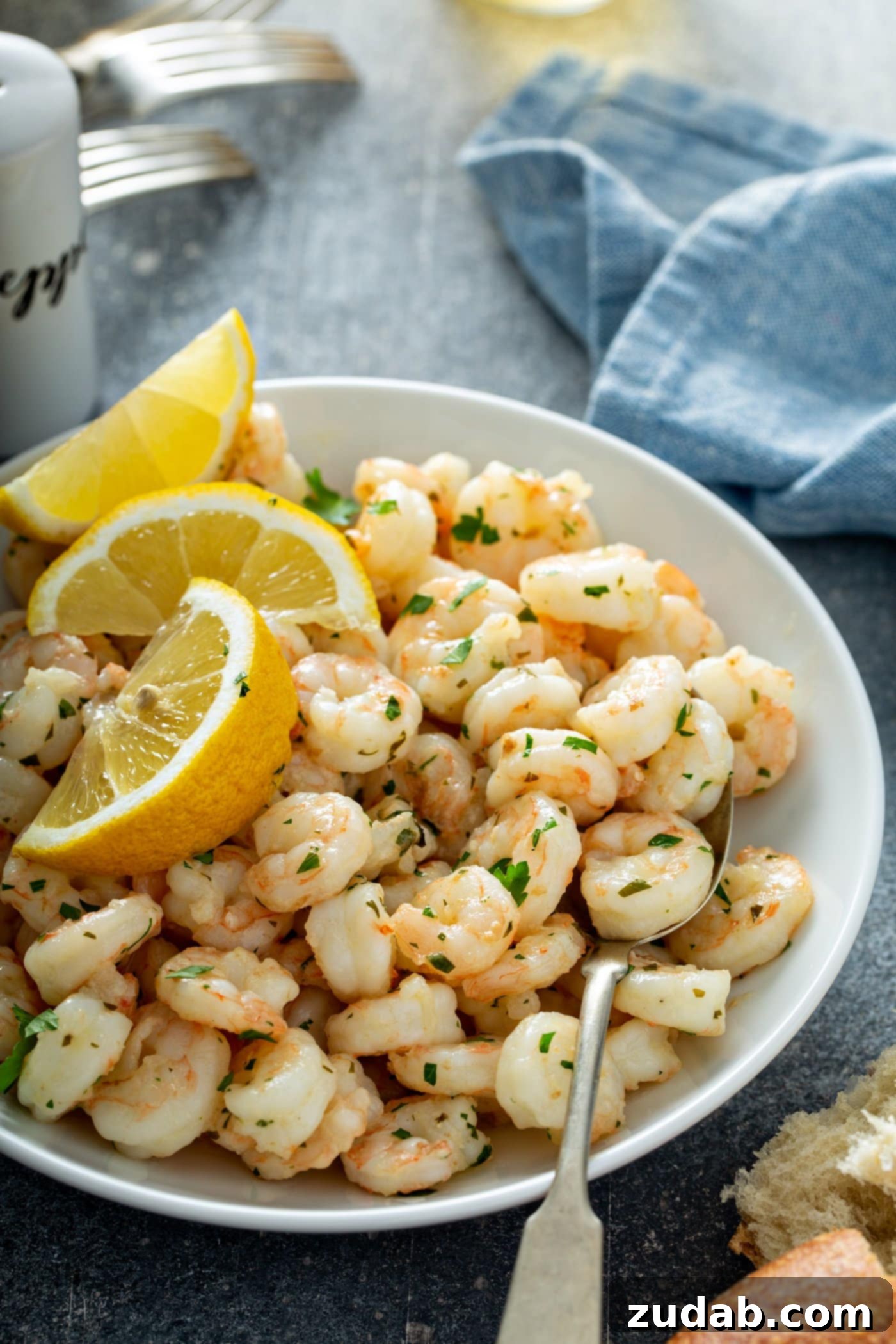 Best Shrimp for Lemon Garlic Shrimp A beautiful serving plate of lemon garlic shrimp, artfully garnished with three bright lemon wedges and a generous scattering of fresh parsley. A crisp napkin and classic salt and pepper shakers are subtly blurred in the background, creating an inviting and complete dining scene.