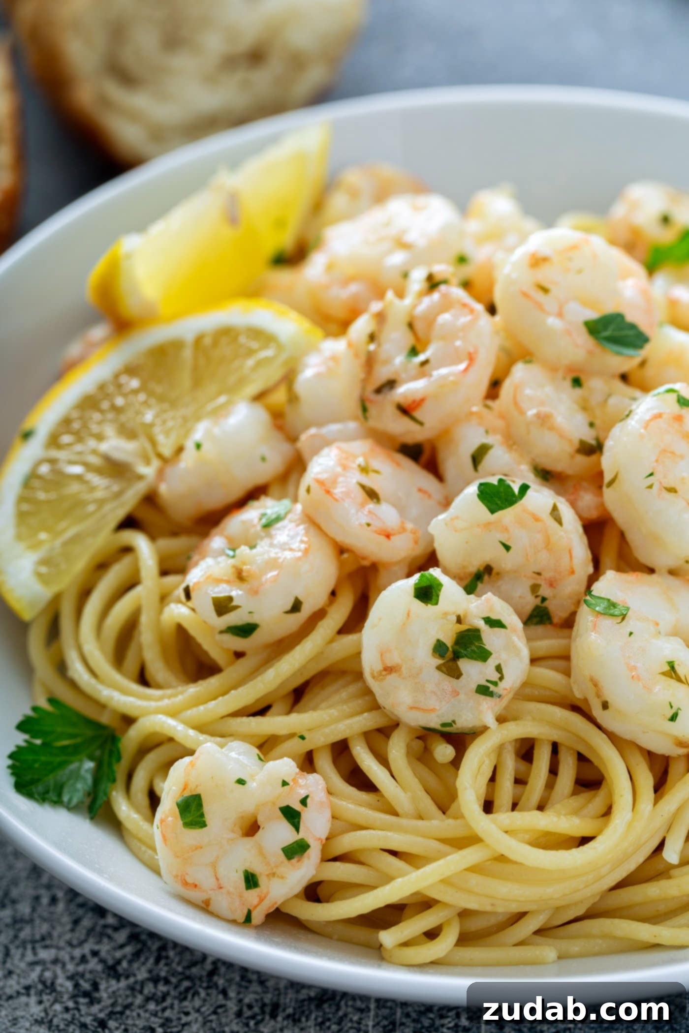 Shrimp Sizing Explained A generous serving of lemon garlic shrimp gracefully plated over a bed of pasta. The shrimp is brightly garnished with fresh parsley, and two vibrant lemon wedges complete the elegant presentation, making for a truly unforgettable and simple seafood dish.