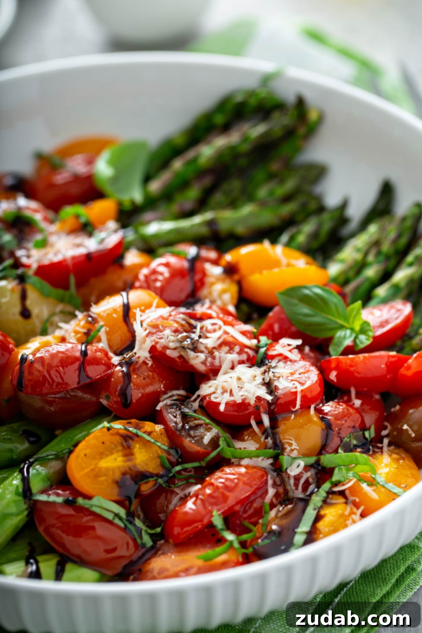 Caramelized Balsamic Asparagus and Tomatoes 2 A close-up picture of balsamic glazed roasted tomatoes and asparagus. The bright green asparagus and sliced red and yellow tomatoes are drizzled with balsamic glaze and topped with grated Parmesan cheese. The rich colors highlight the freshness of the ingredients, making it an enticing and healthy side dish for any meal.
