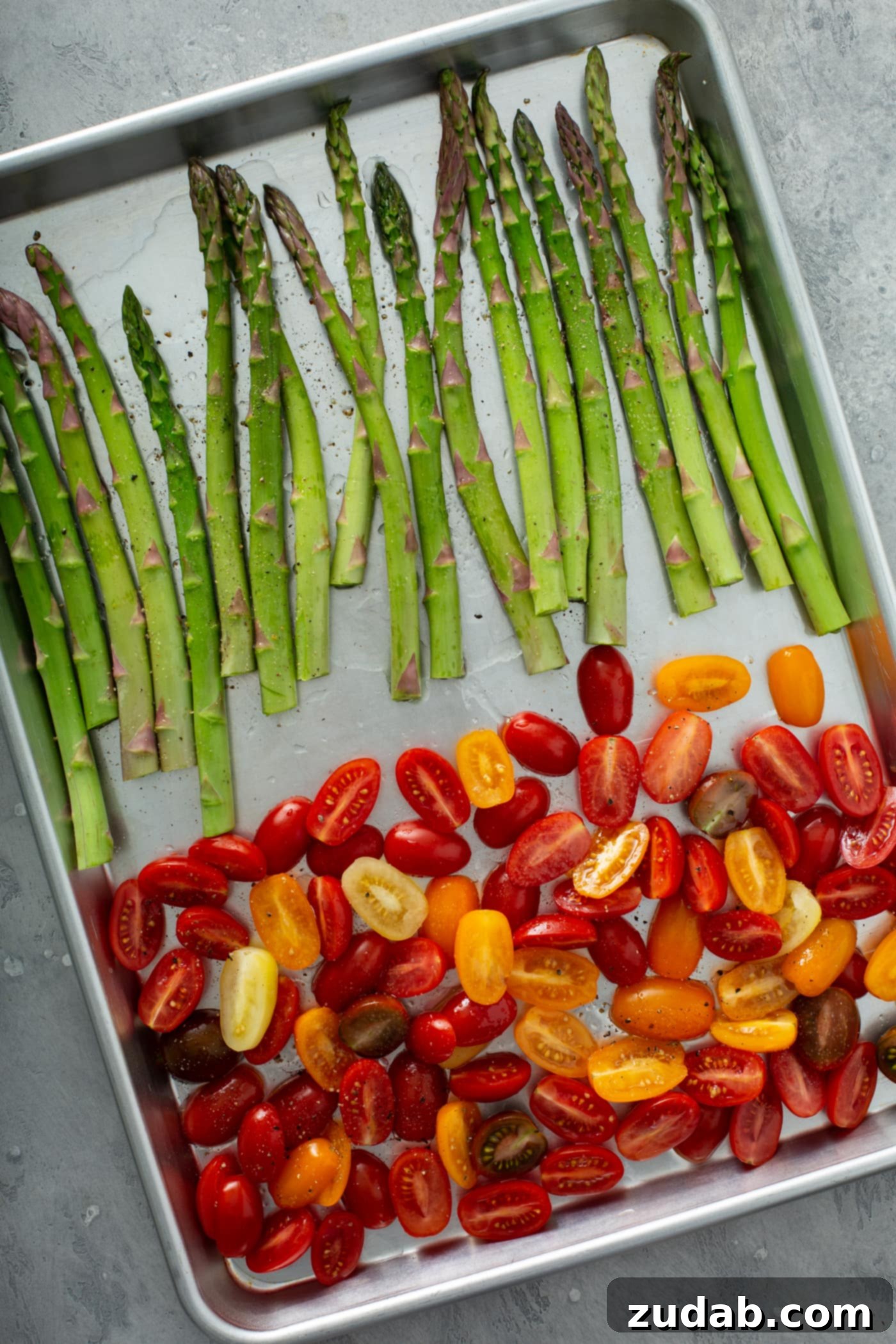 Caramelized Balsamic Asparagus and Tomatoes 4 A baking pan with fresh green asparagus on one end and sliced red and yellow heirloom tomatoes on the other end, lightly tossed with oil, salt, and pepper, ready for roasting.