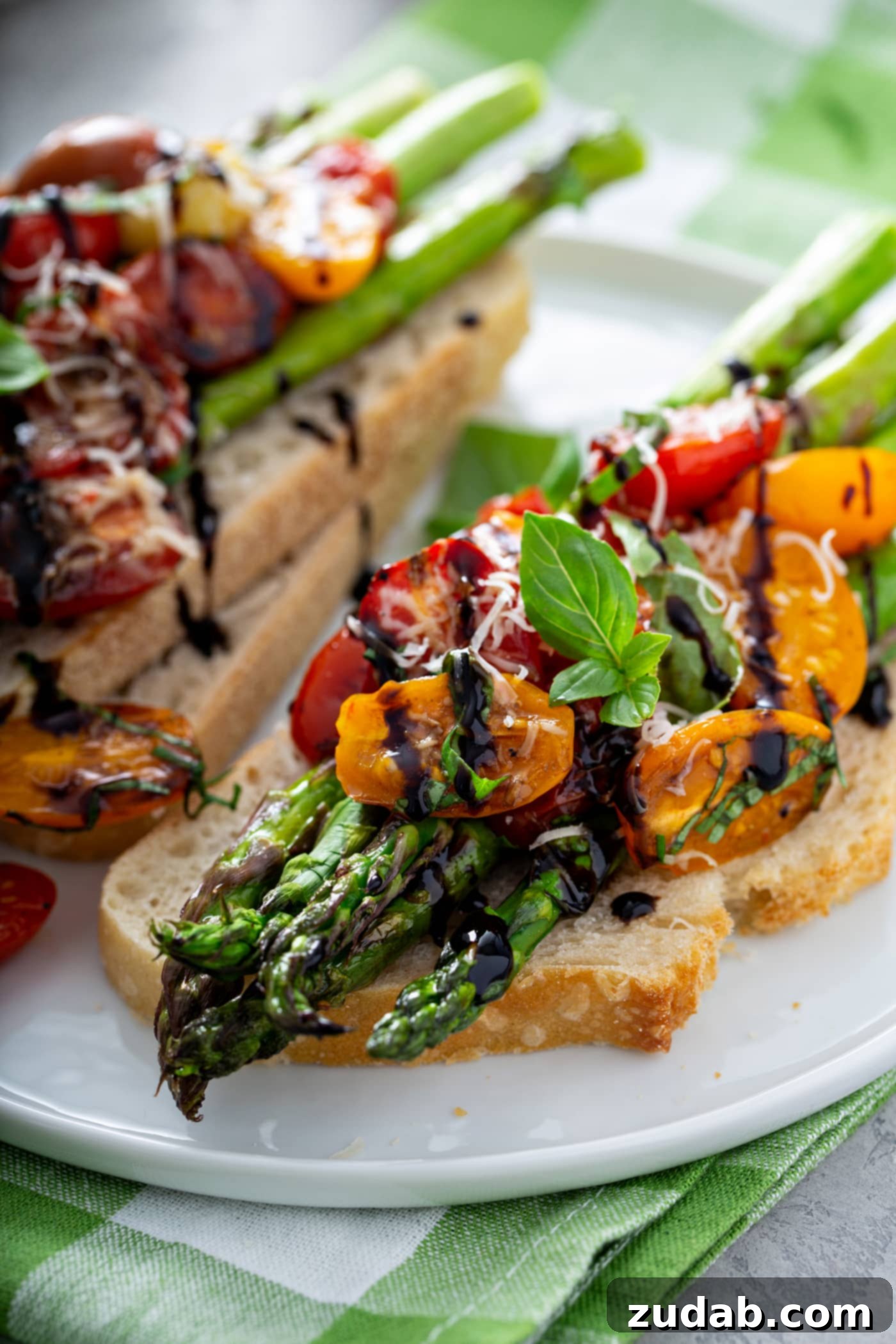Caramelized Balsamic Asparagus and Tomatoes 6 A serving of balsamic glazed roasted tomatoes and asparagus on a slice of toasted bread. The roasted tomatoes and asparagus are drizzled with balsamic glaze and sprinkled with grated Parmesan cheese. There is another serving on two slices of bread in the background, suggesting a versatile way to enjoy this side dish.