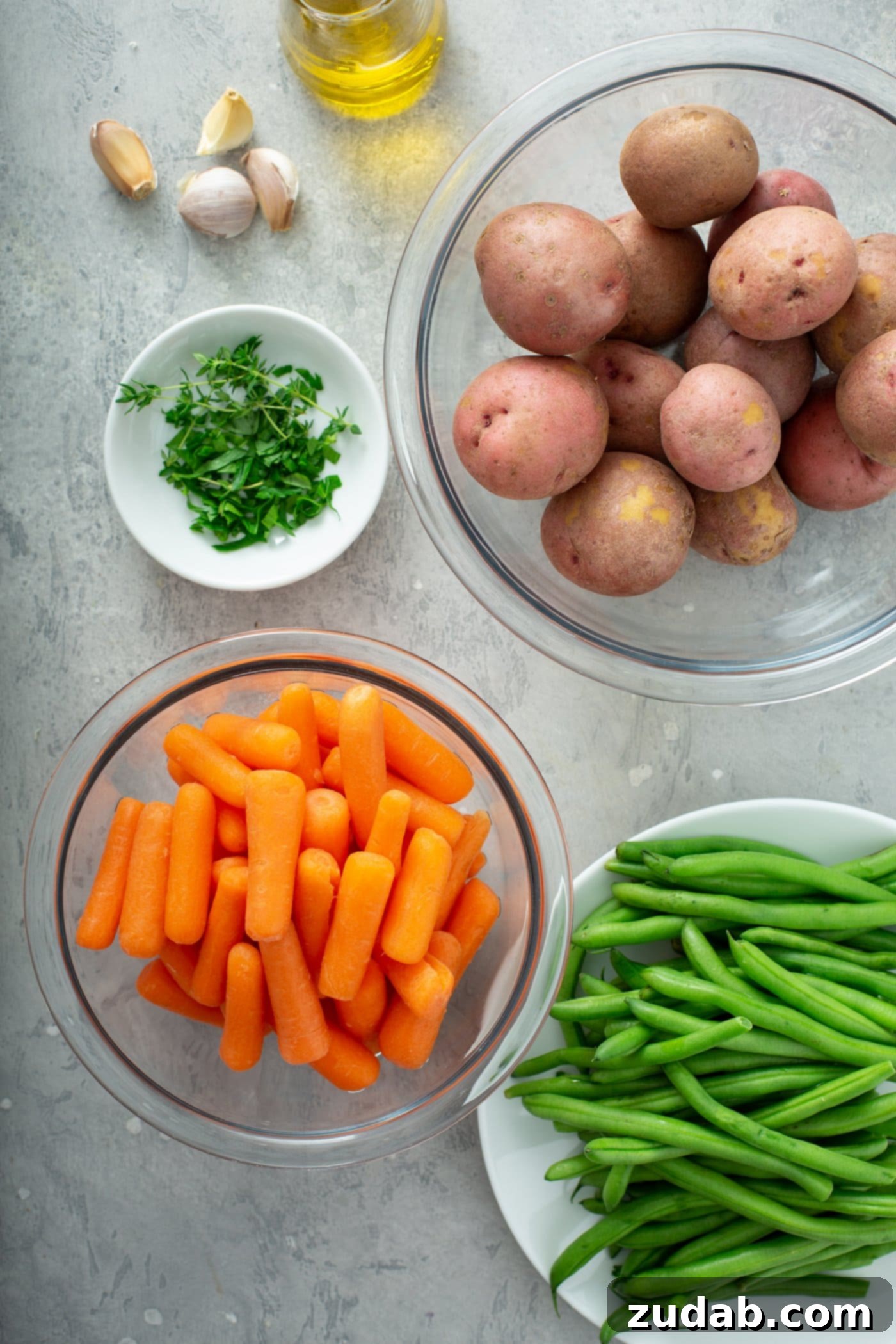 Bowls containing red potatoes, baby carrots, fresh green beans, and fresh green herbs.