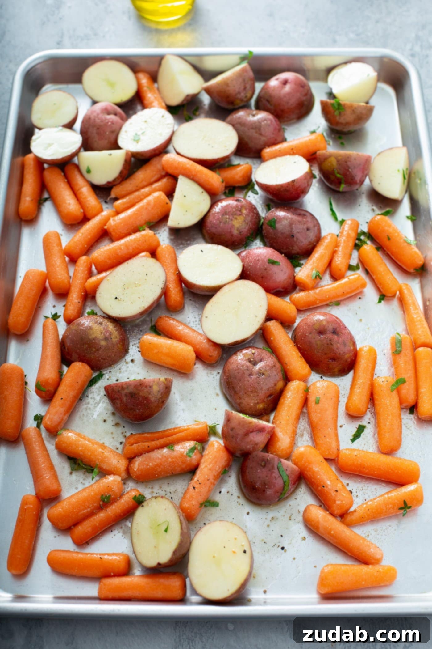 A sheet pan containing red potatoes that are cut in half and baby carrots.