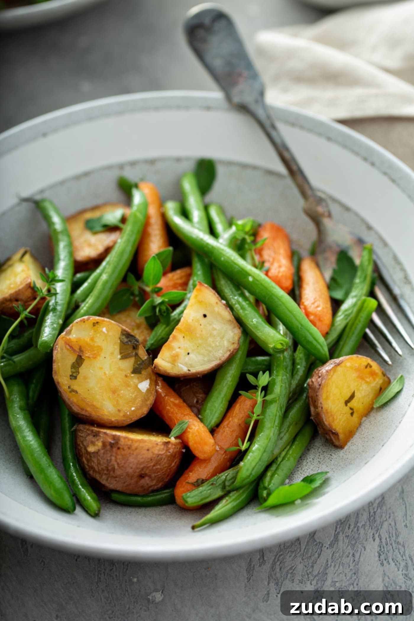 A plate filled with roasted red potatoes, baby carrots, and fresh green beans. A fork is resting next to the roasted vegetables.
