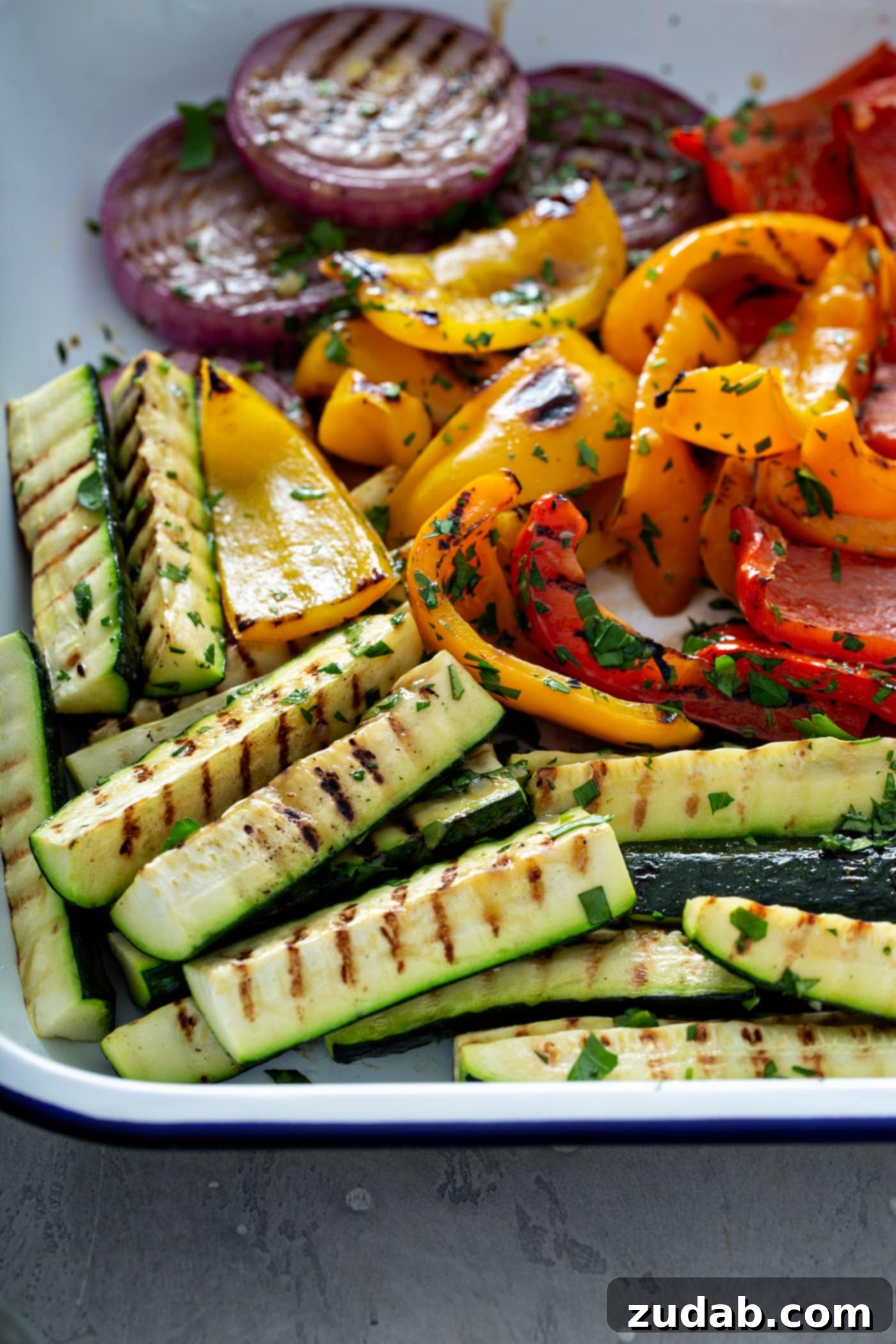 Grilled Vegetables with Balsamic Vinaigrette 11 A generous plate overflowing with perfectly grilled vegetables, featuring tender zucchini wedges, sweet red onion slices, and colorful red and yellow bell peppers, all marked with enticing grill lines and lightly sprinkled with fresh parsley leaves.