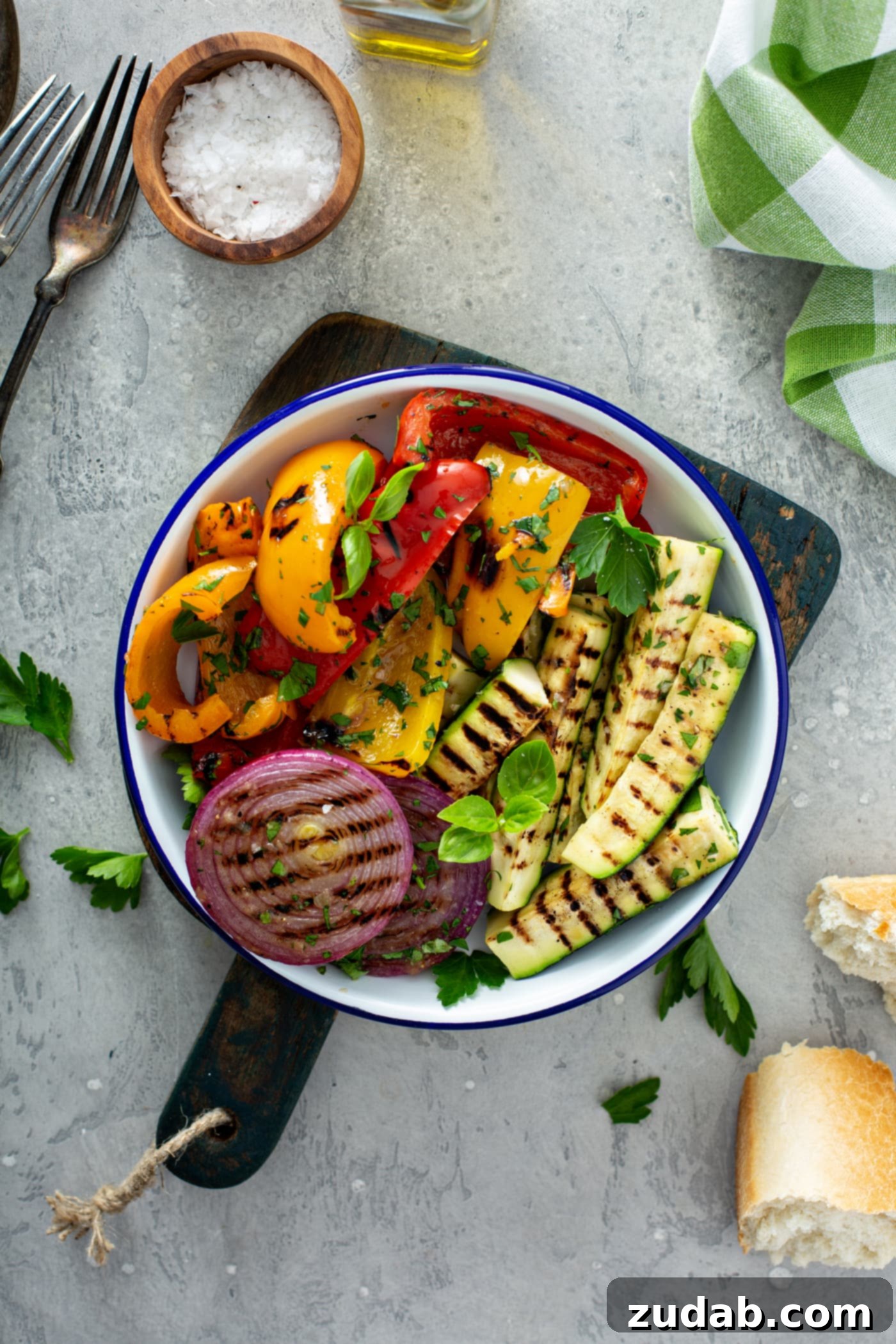 Grilled Vegetables with Balsamic Vinaigrette 13 A rustic wooden cutting board holds a serving plate piled high with grilled vegetables, including tender red onion, vibrant red and yellow bell peppers, and succulent zucchini, all garnished with fresh parsley leaves. More parsley leaves are scattered on the table, adding to the fresh appeal.