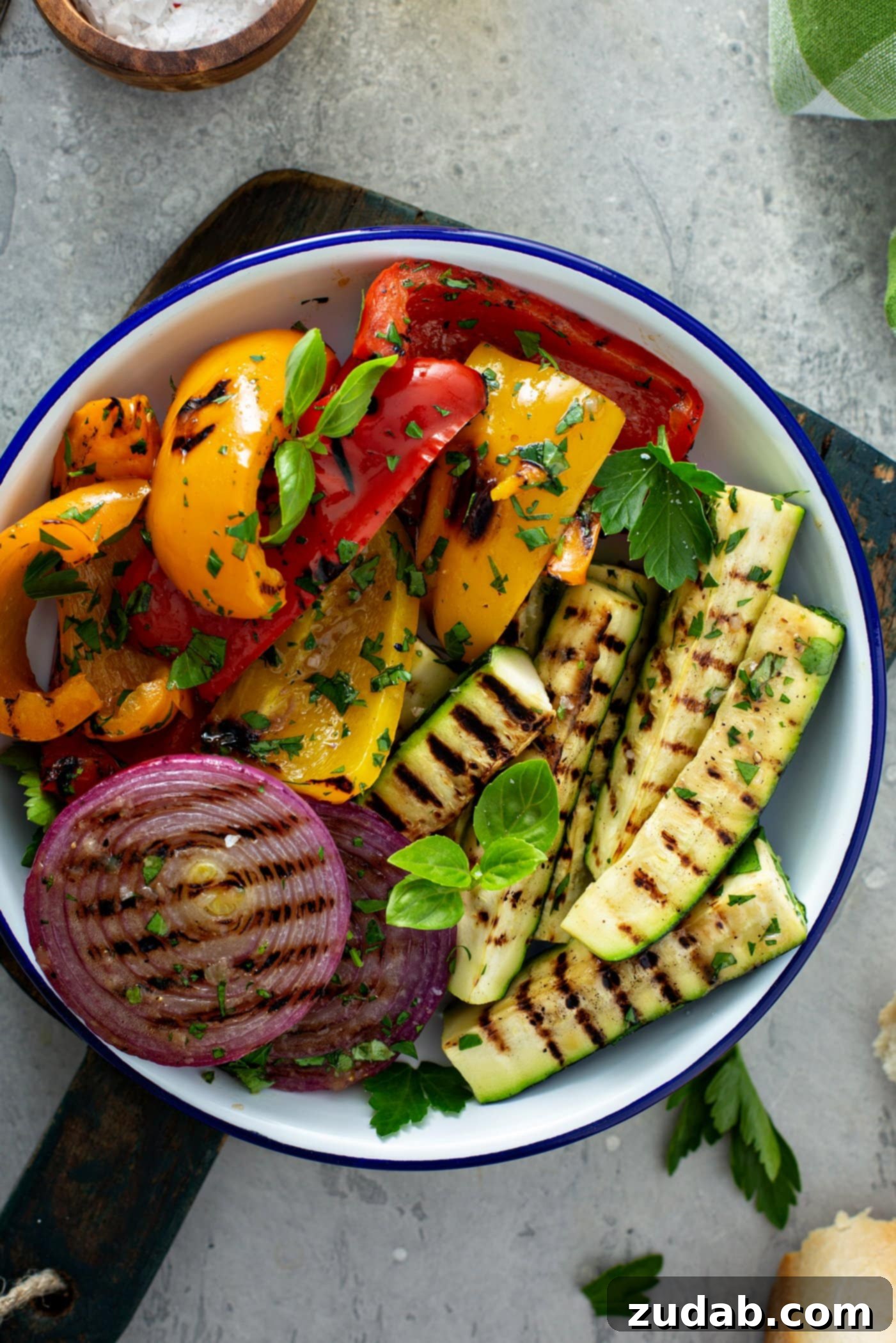 Grilled Vegetables with Balsamic Vinaigrette 14 A generous serving dish displays a medley of grilled vegetables: tender red onion slices, perfectly charred zucchini wedges, and vibrant red and yellow bell peppers, all highlighted by light brown grill marks and garnished with fresh parsley leaves.