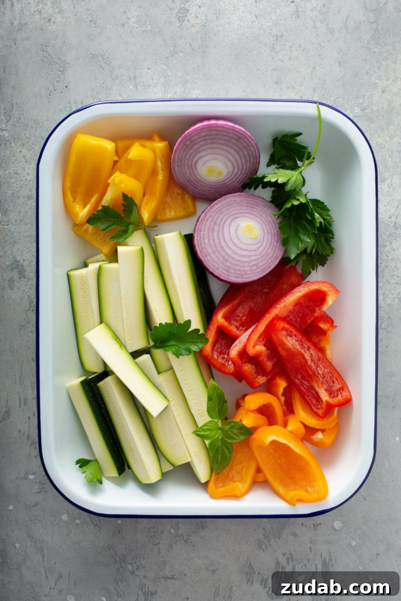Grilled Vegetables with Balsamic Vinaigrette 5 A colorful plate featuring fresh, uncooked zucchini wedges, thinly sliced red onion, vibrant red and yellow bell pepper strips, and a scattering of fresh parsley leaves, ready for grilling and dressing.