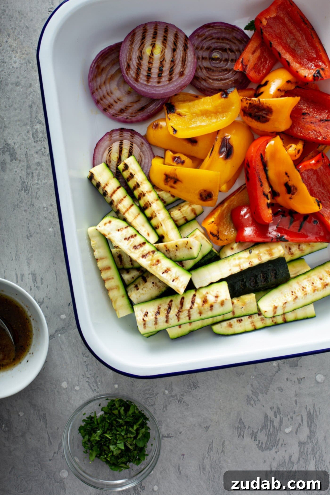 Grilled Vegetables with Balsamic Vinaigrette 6 A vibrant plate of grilled zucchini wedges, sliced red onion, and colorful red and yellow bell peppers, all adorned with beautiful grill marks. A small glass cup of balsamic glaze sits invitingly beside the plate, ready for drizzling.