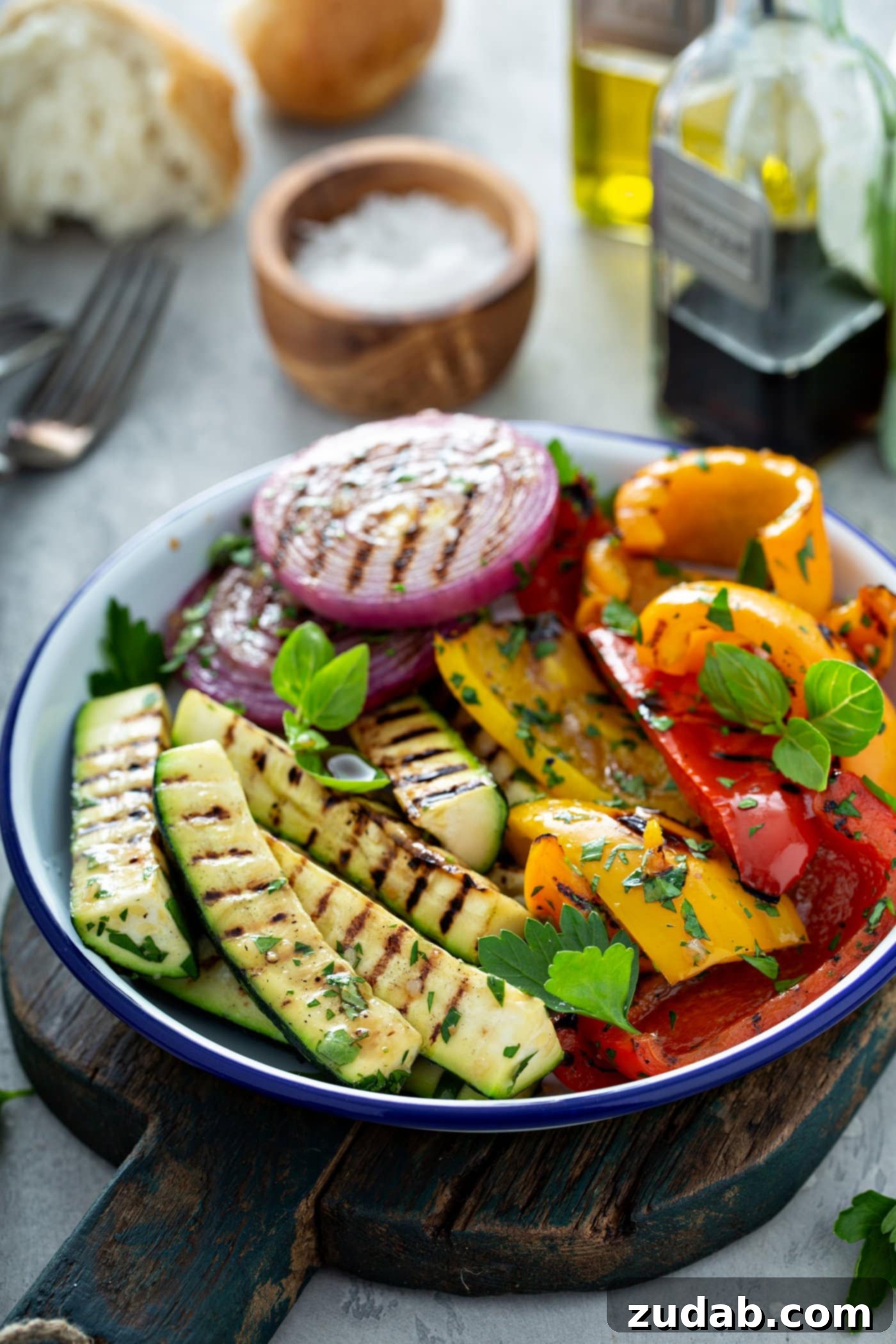 Grilled Vegetables with Balsamic Vinaigrette 10 A stunning plate of grilled vegetables, showcasing tender zucchini, vibrant bell peppers, and sweet red onions, all with beautifully defined grill marks and garnished with fresh parsley. In the background, a small wooden bowl of salt, a fork, and a glass cup of balsamic glaze complete the inviting culinary scene.