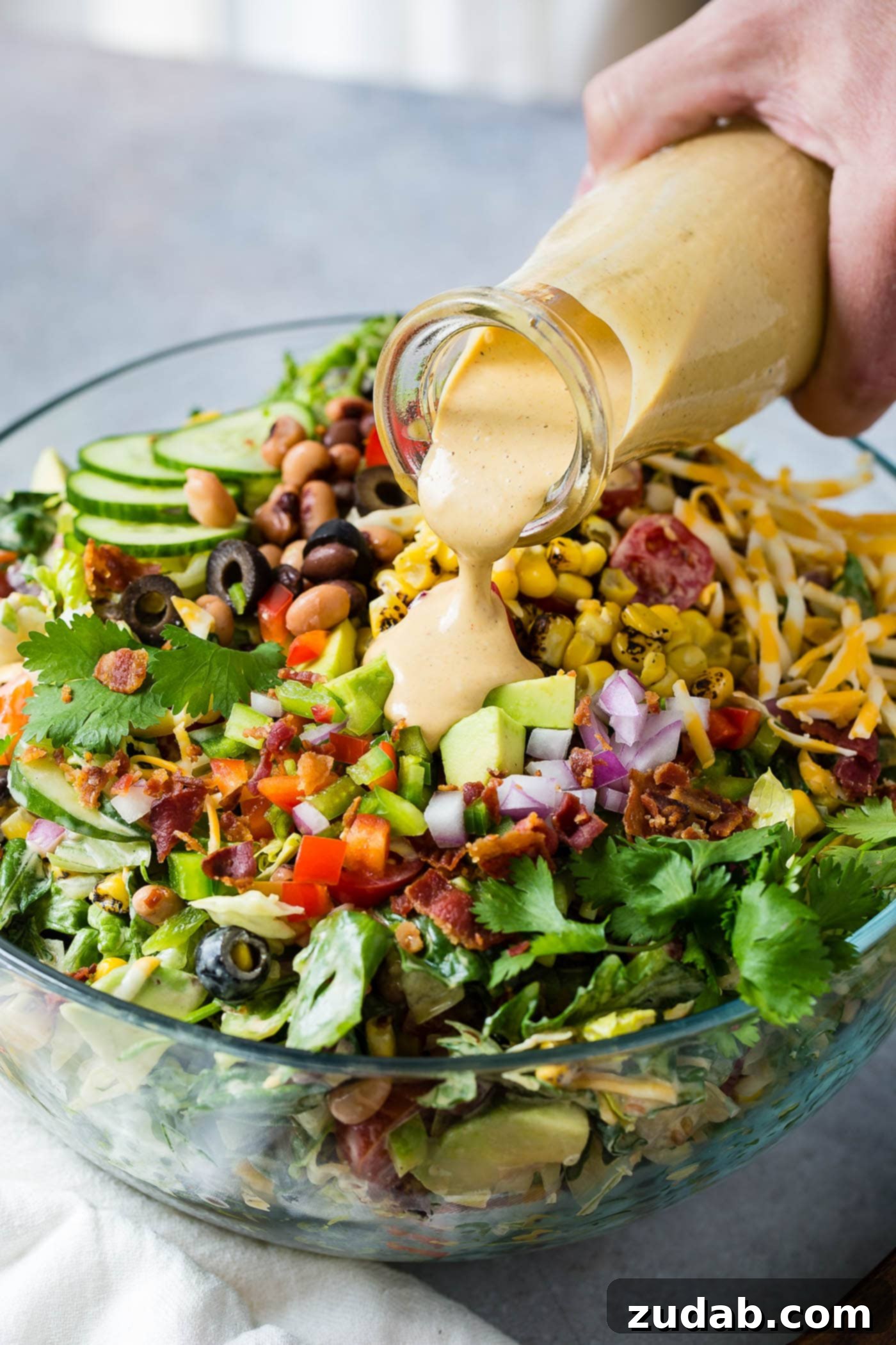 Chuckwagon Salad 2 Cowboy salad in a serving bowl. A special dressing is being poured over the chopped onions, tomatoes, bacon, avocados, beans and lettuce.