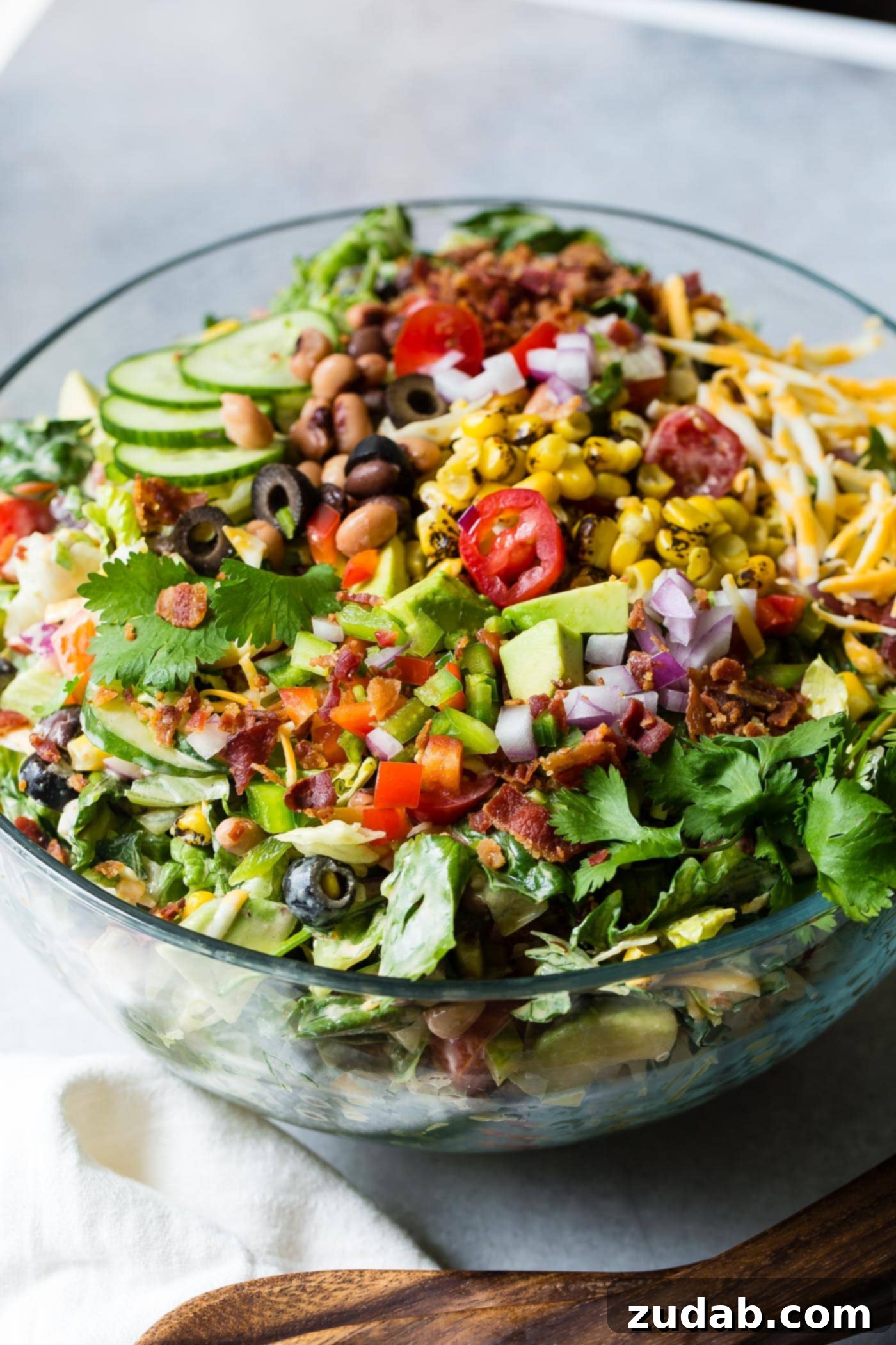 Chuckwagon Salad 3 Cowboy salad that is all mixed up and ready to eat. There are sliced cucumbers, chopped tomatoes, chopped avocados, corn, beans, red onions, shredded cheese and green lettuce.
