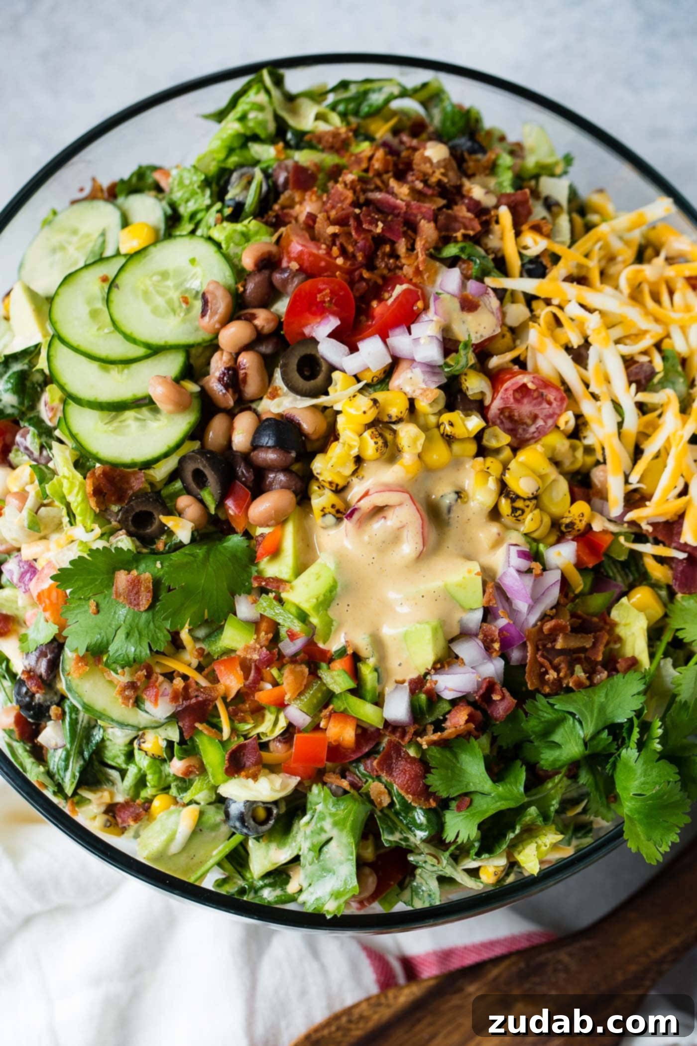 Chuckwagon Salad 5 A top view of cowboy salad in a glass serving bowl. There are sliced cucumbers, sliced olives, chopped tomatoes, avocados, lettuce and green onions. It contains corn and beans too and is topped with dressing.