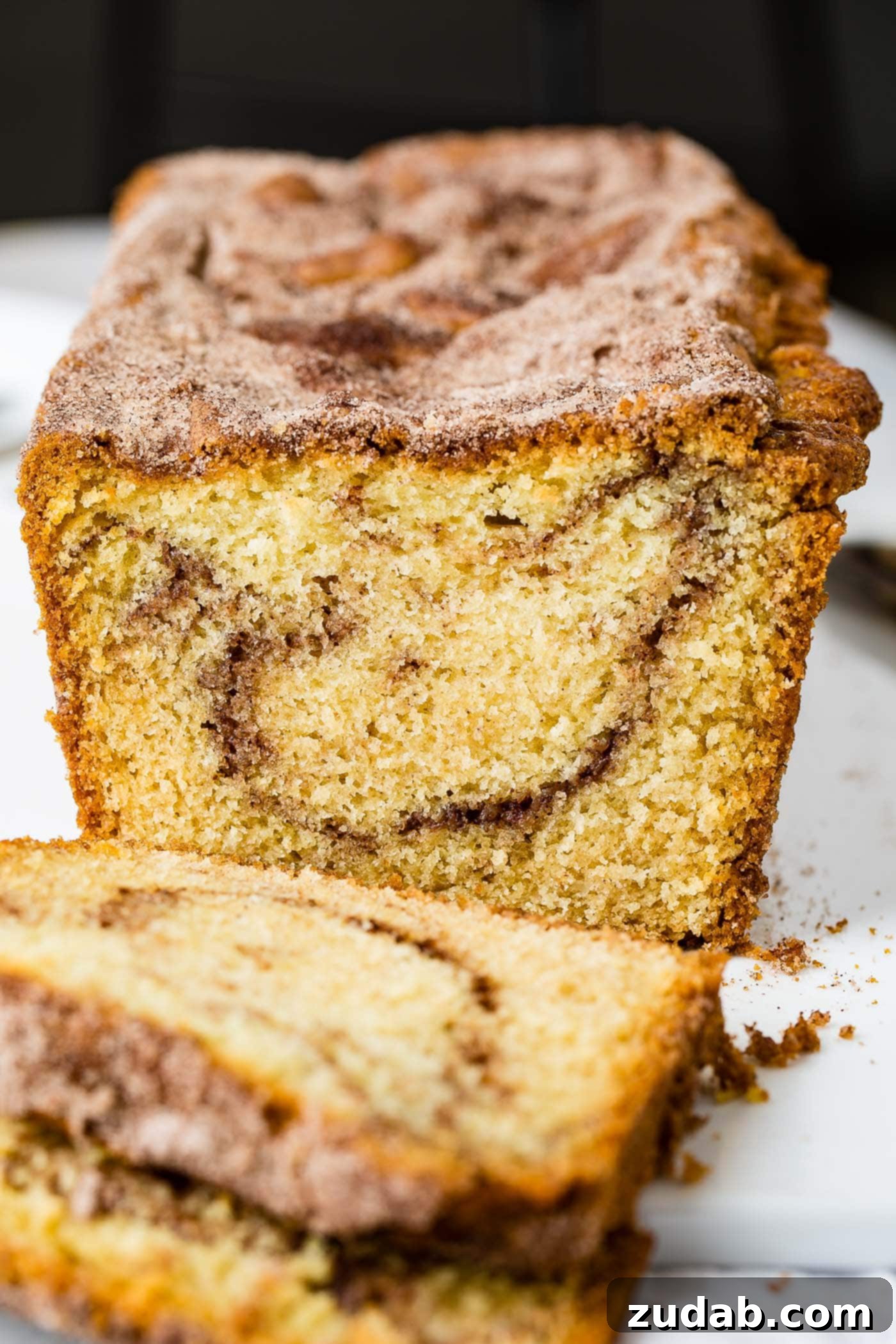 Snickerdoodle Swirl Bread 2 A beautifully baked loaf of Snickerdoodle Bread, partially sliced to reveal a delicate swirl of cinnamon sugar within. The top crust is golden brown and sprinkled with cinnamon sugar.