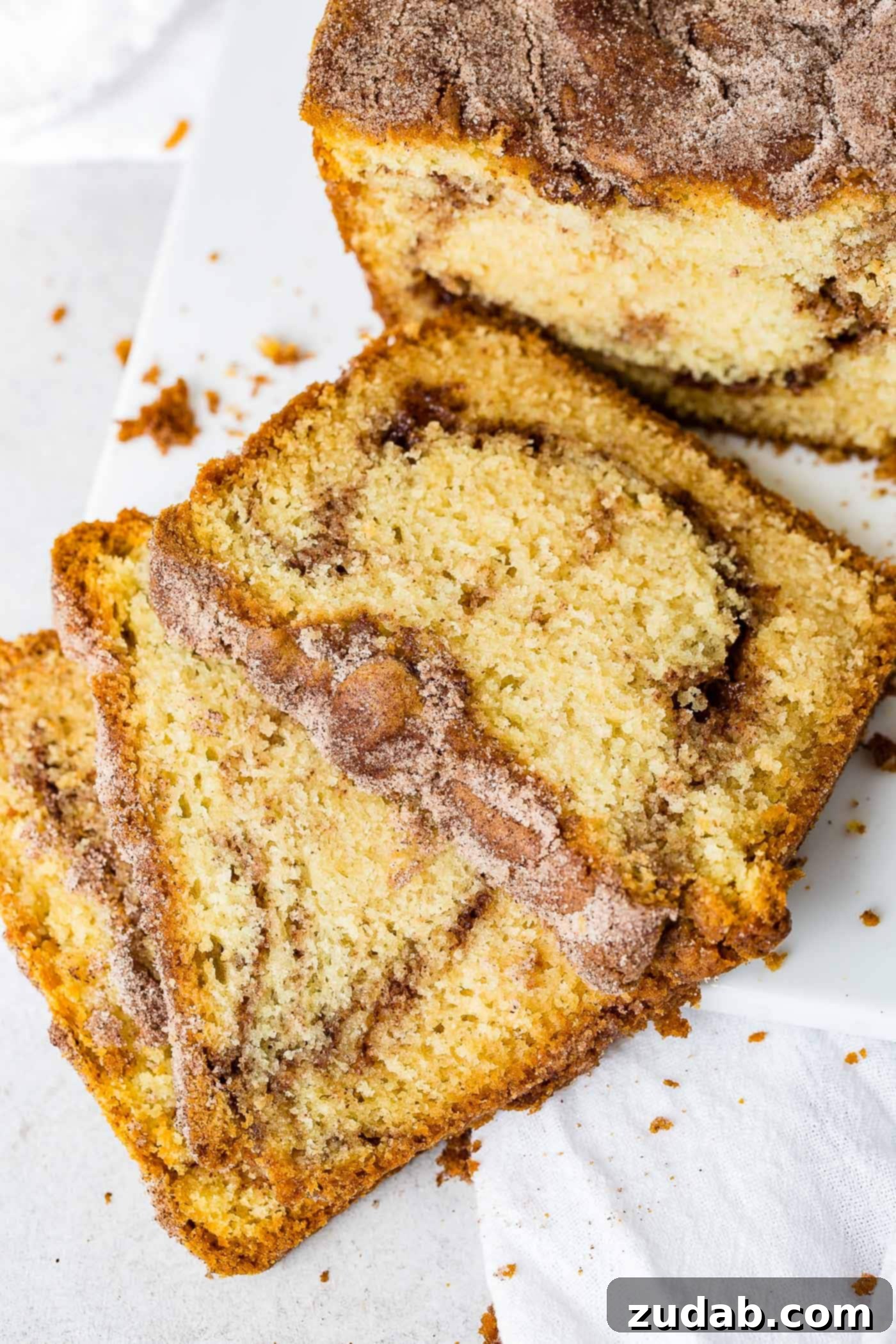 Snickerdoodle Swirl Bread 3 Three perfectly cut slices of Snickerdoodle Bread arranged on a plate, showcasing the distinct cinnamon sugar swirl. The remainder of the golden-brown loaf sits in the background.
