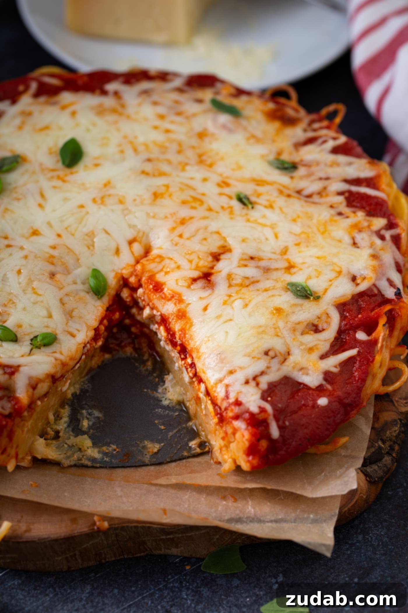Baked Spaghetti Pie A baked spaghetti pie with a single slice meticulously removed, revealing the delightful layers within. The layers clearly show the spaghetti noodle base, a rich, savory spaghetti sauce, and a generous topping of melted, shredded cheese. A delicate sprinkle of fresh basil leaves adorns the surface, adding a touch of freshness and color to the comforting dish.