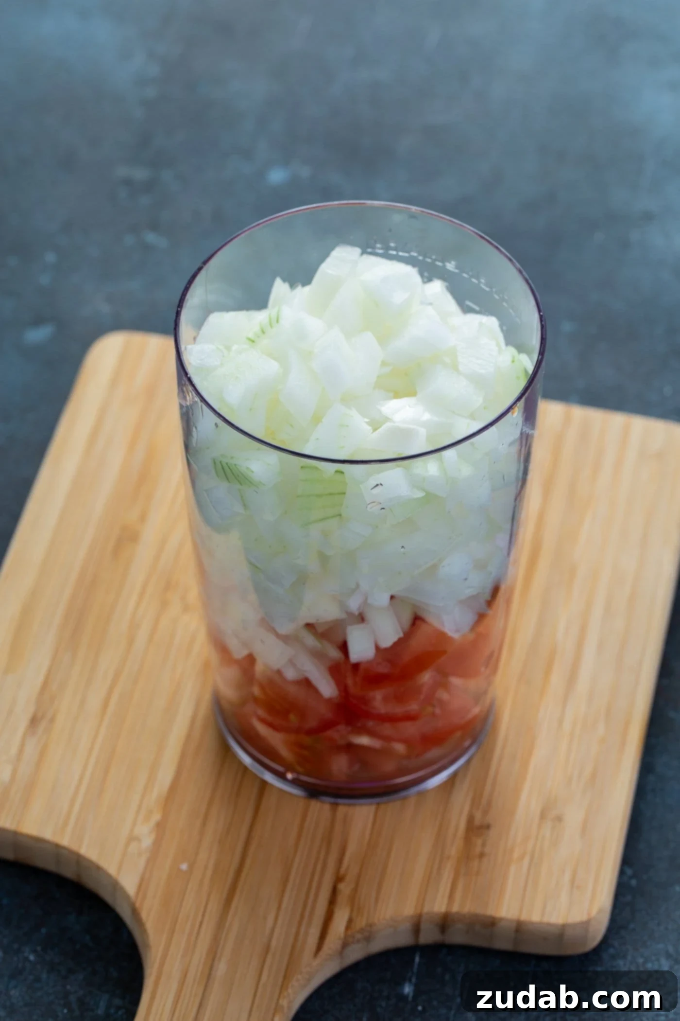 A glass container of a layer of chopped tomatoes and chopped onions on top.