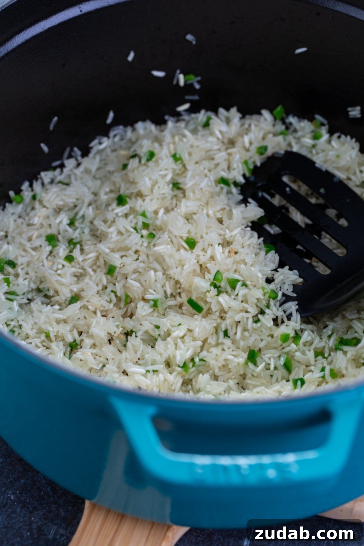 A bowl of fluffy white rice with chopped cilantro in it. A wooden spoon rests on top of the rice.