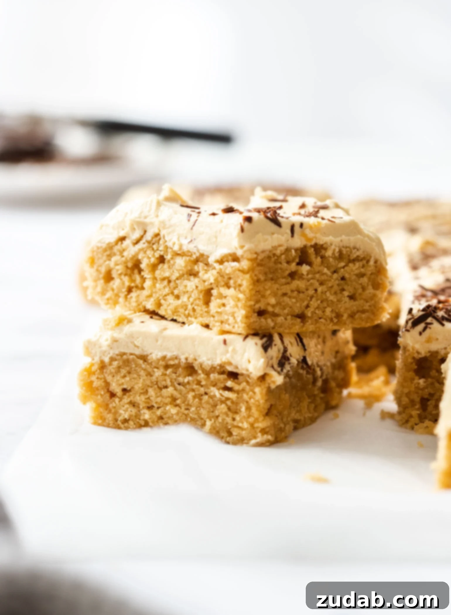 Ultimate Peanut Butter Sheet Cake 2 Two generous slices of peanut butter sheet cake, one resting atop the other, showcasing the fluffy cake and creamy frosting layers. The top slice is garnished with delicate chocolate shavings, hinting at a perfect flavor combination.