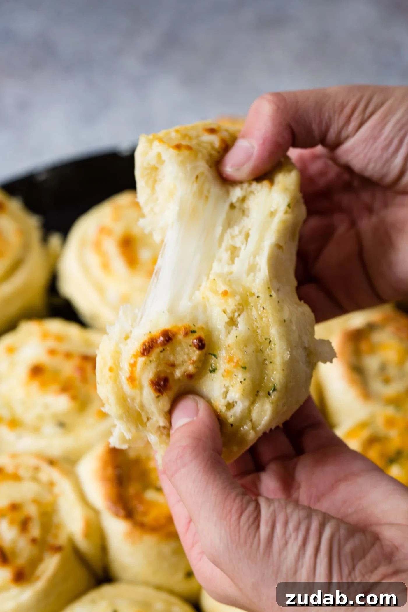 Golden Cheesy Perfection 5 A cheese doodle being pulled apart so you can see the melty mozzarella cheese in side. The bread is golden brown and a pan full of cheese doodles are below it.
