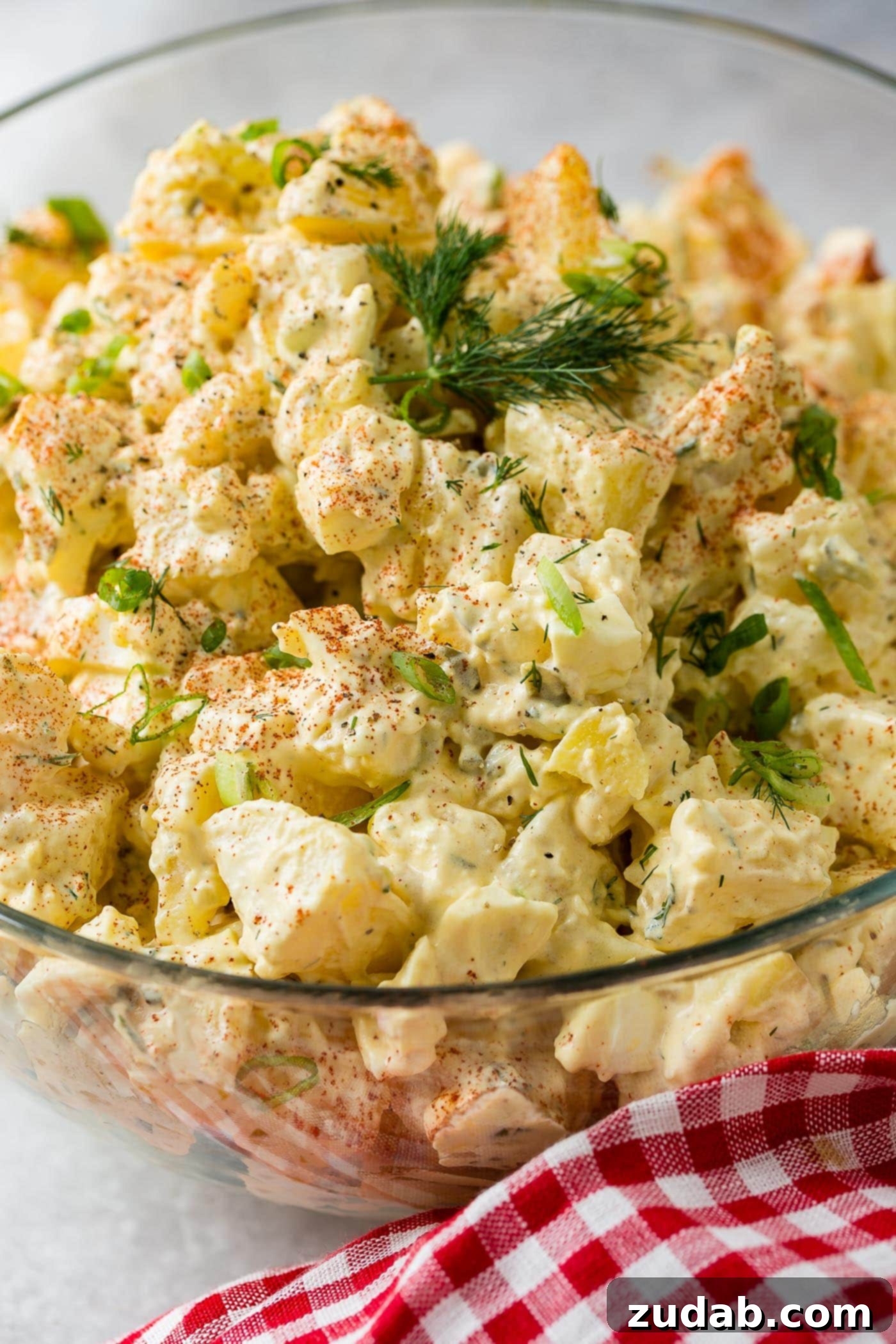 Secrets to the Best Potato Salad Ever 4 A glass bowl of potato salad. The chunks of potato, pickles, and eggs are mixed together in a perfect dressing. The salad is sprinkled with paprika and fresh parsley.